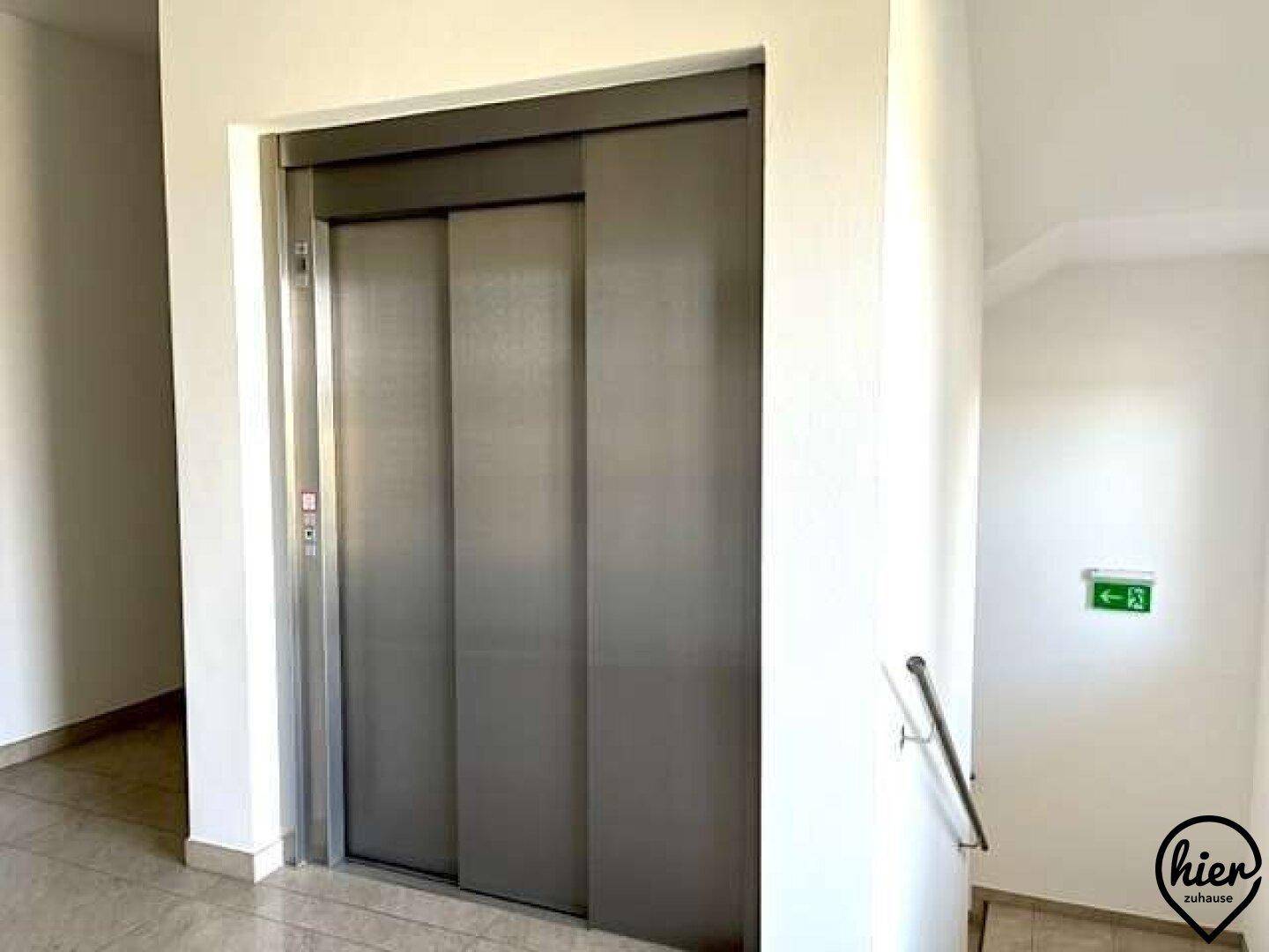 Flur mit einem Aufzug und einem Treppenhaus mit Handläufen, die den Zugang erleichtern.