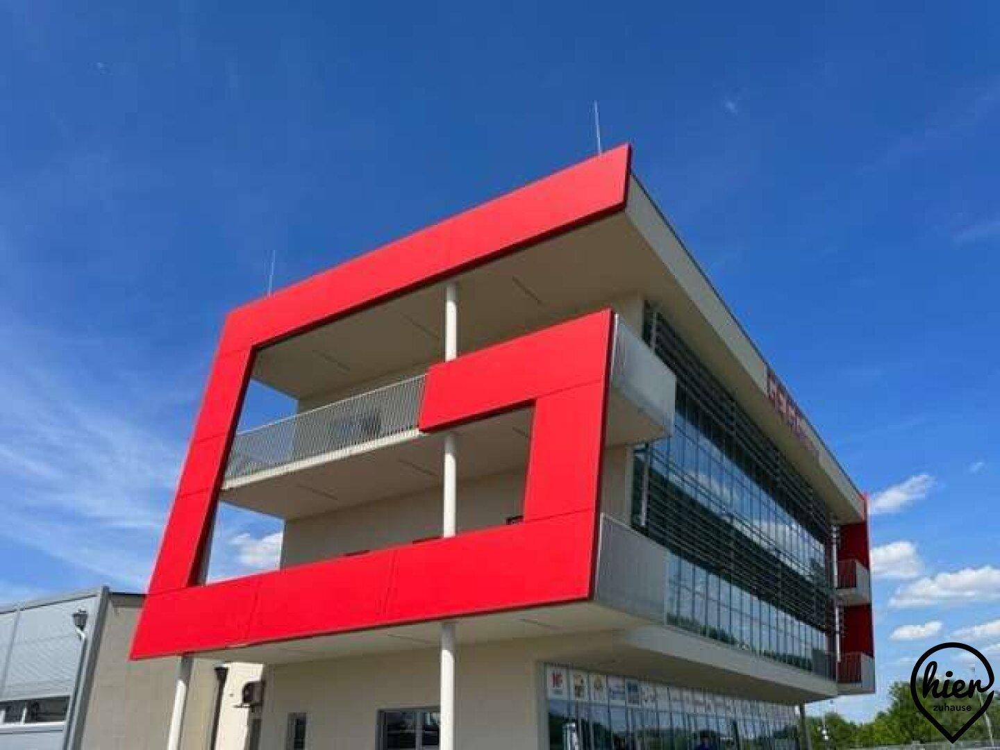 Modernes Gebäude mit auffälligen roten Rahmen und großen Glasflächen, aus einer unteren Perspektive aufgenommen.