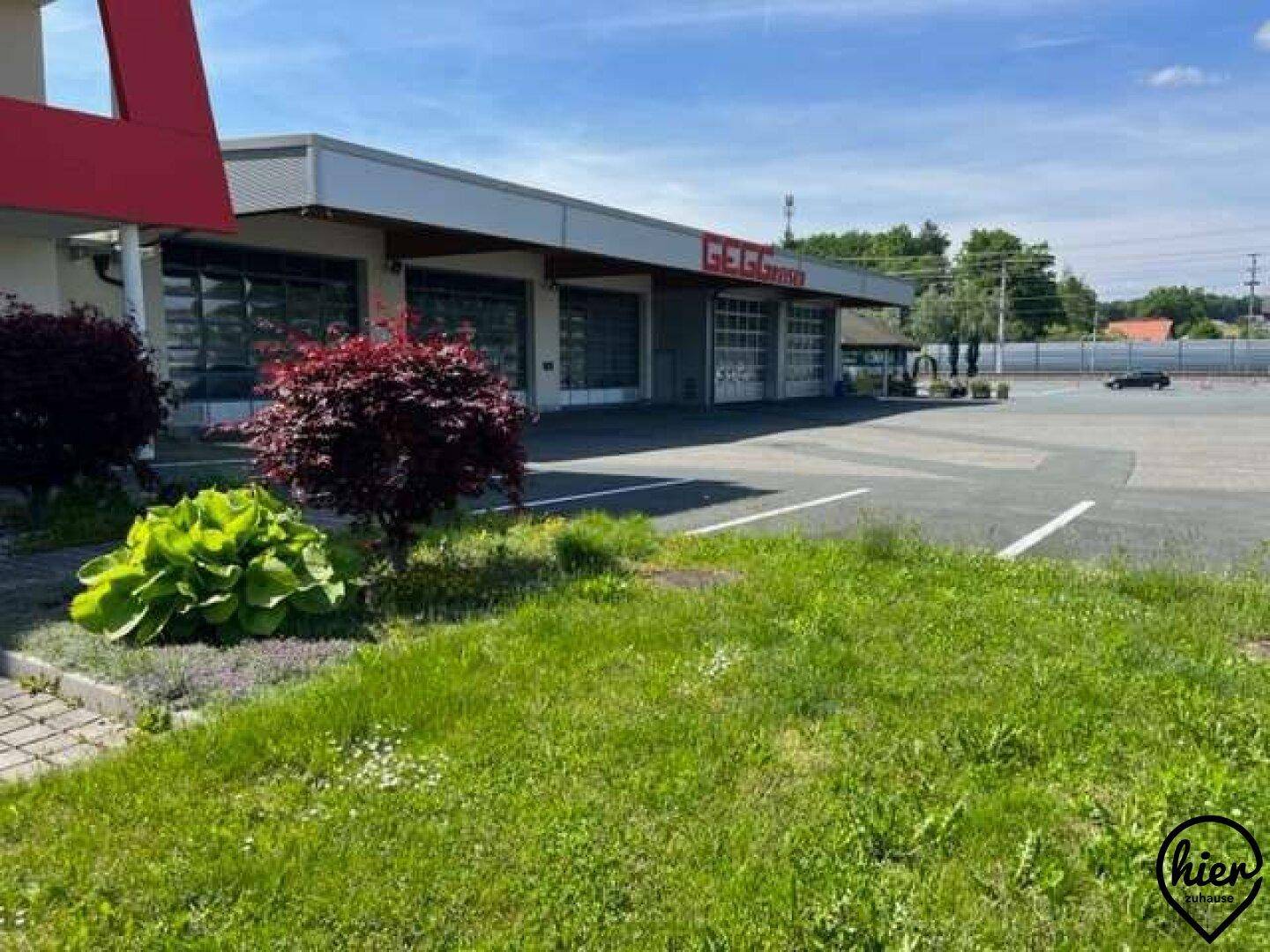 Gewerbegebäude mit Garagentoren, einer kleinen Grünfläche und einem angrenzenden Parkplatz.