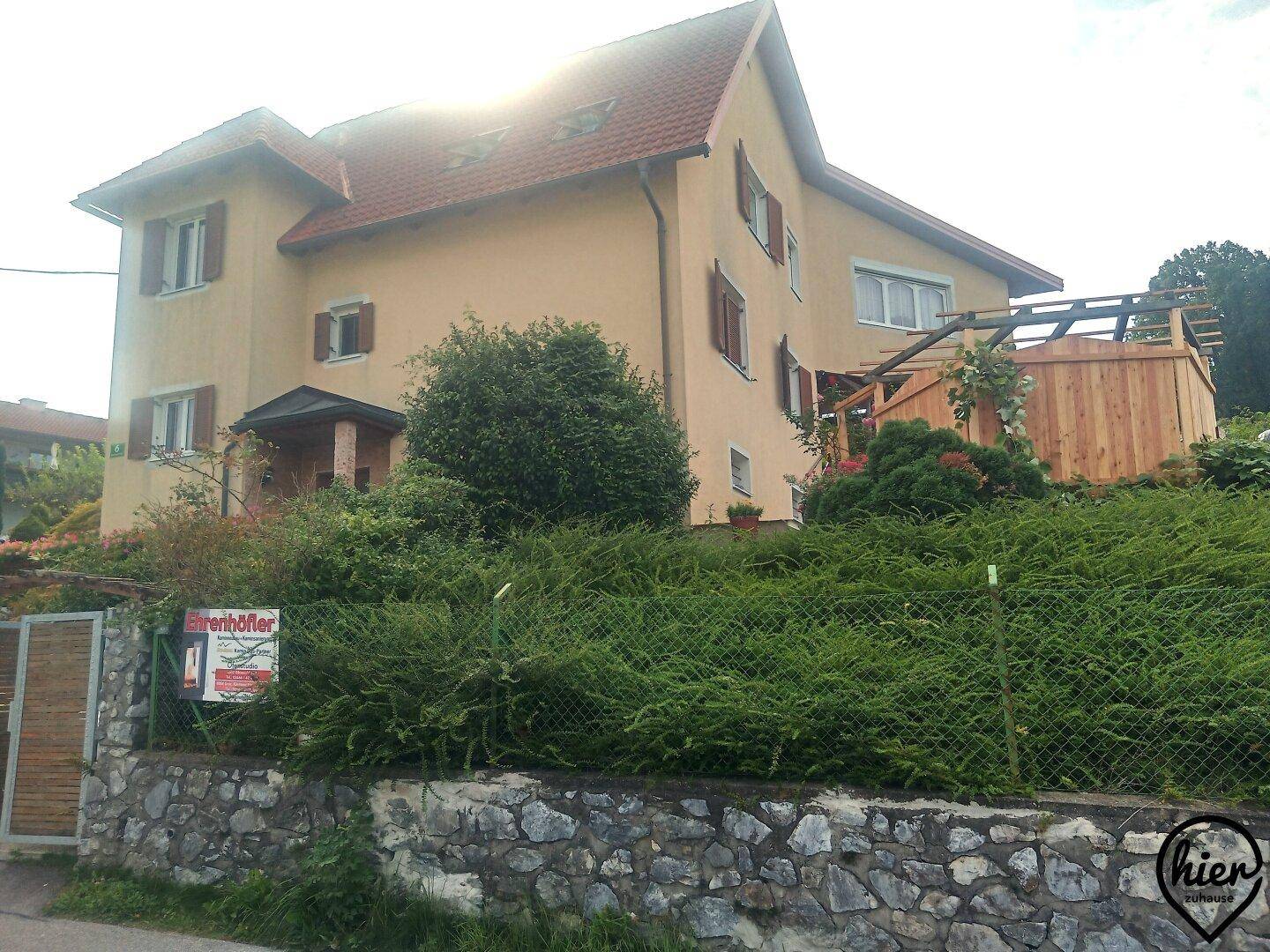 Gelb gestrichenes Einfamilienhaus mit Satteldach und grüner Hecke im Vorgartenbereich.