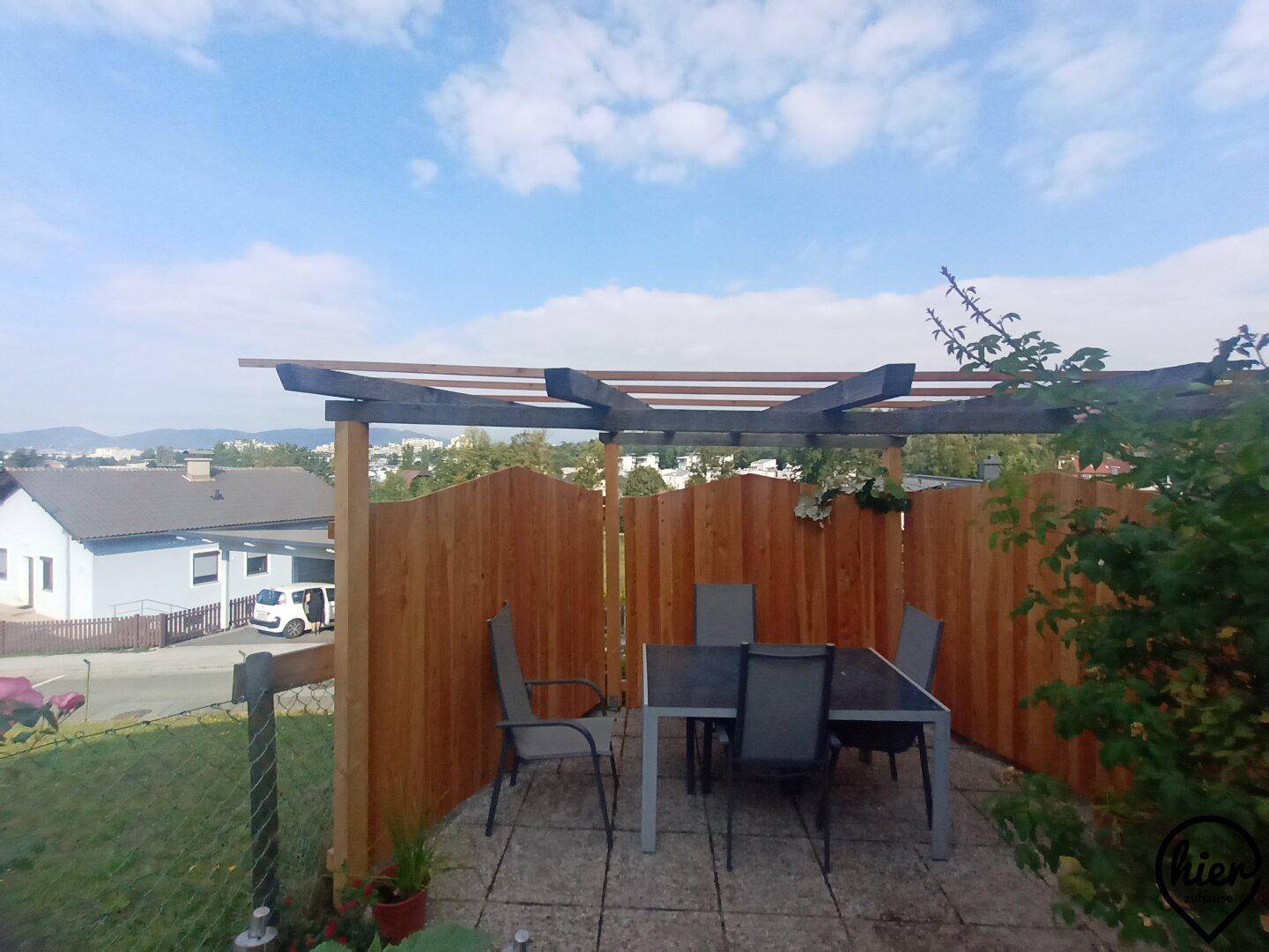 Gepflasterte Terrasse mit Gartenmöbeln, Holzpergola und Blick auf die Umgebung.