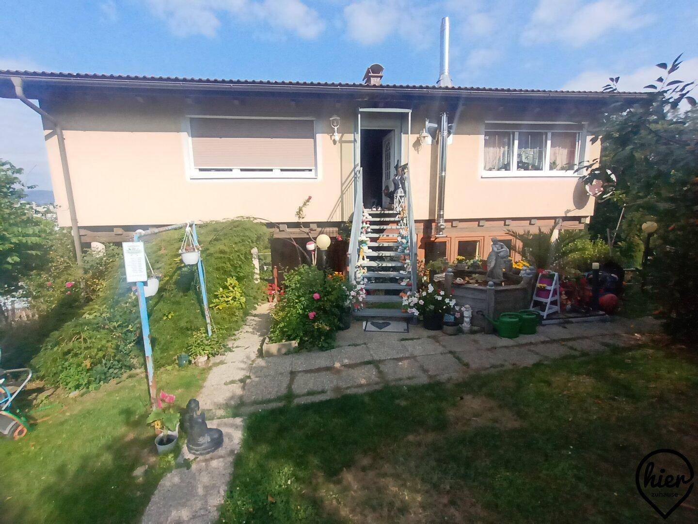 Rückseite des Hauses mit Außentreppe, die zu einem blühenden Gartenbereich führt.