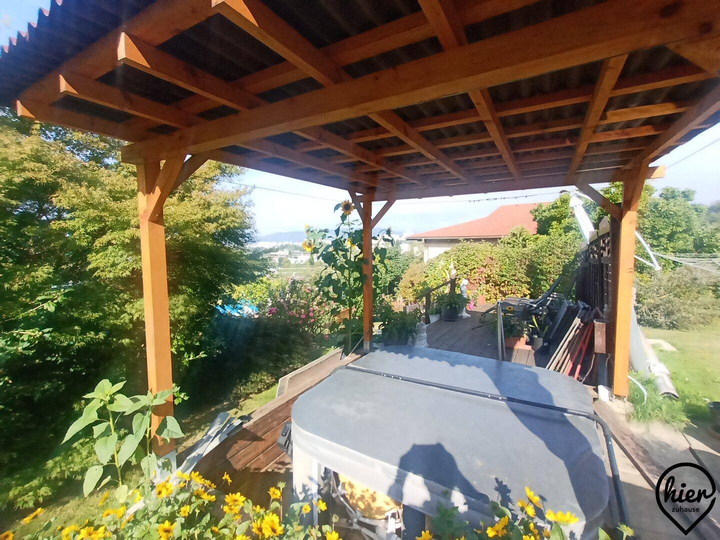 Überdachter Außenbereich mit Holzbalkenkonstruktion und einem Whirlpool im Garten.