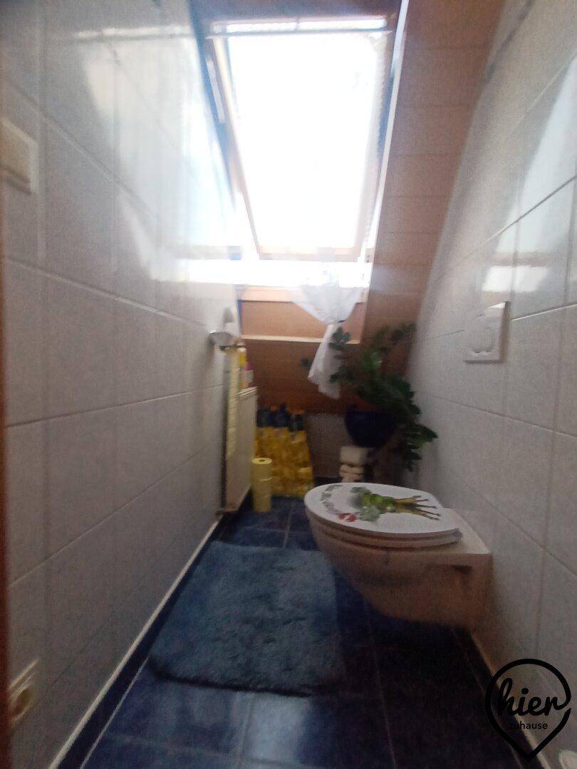 Kleines WC mit Dachfenster und blauen Bodenfliesen unter einer Dachschräge.