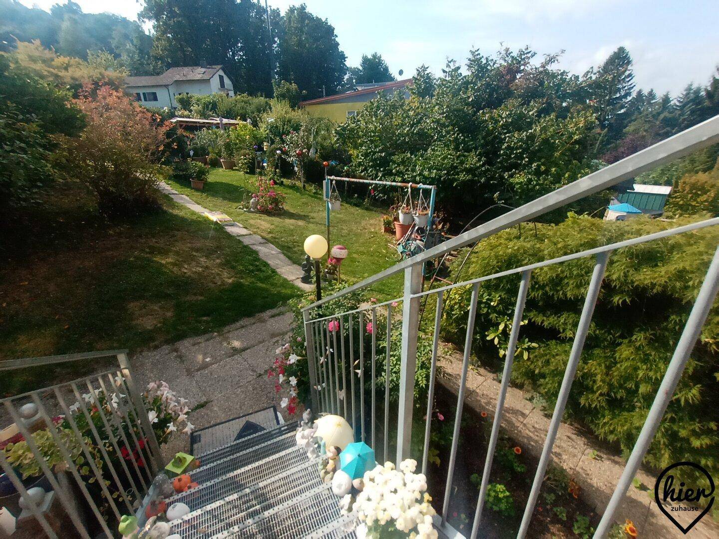 Außentreppe führt hinunter in einen weitläufigen, blühenden Gartenbereich mit viel Grün.
