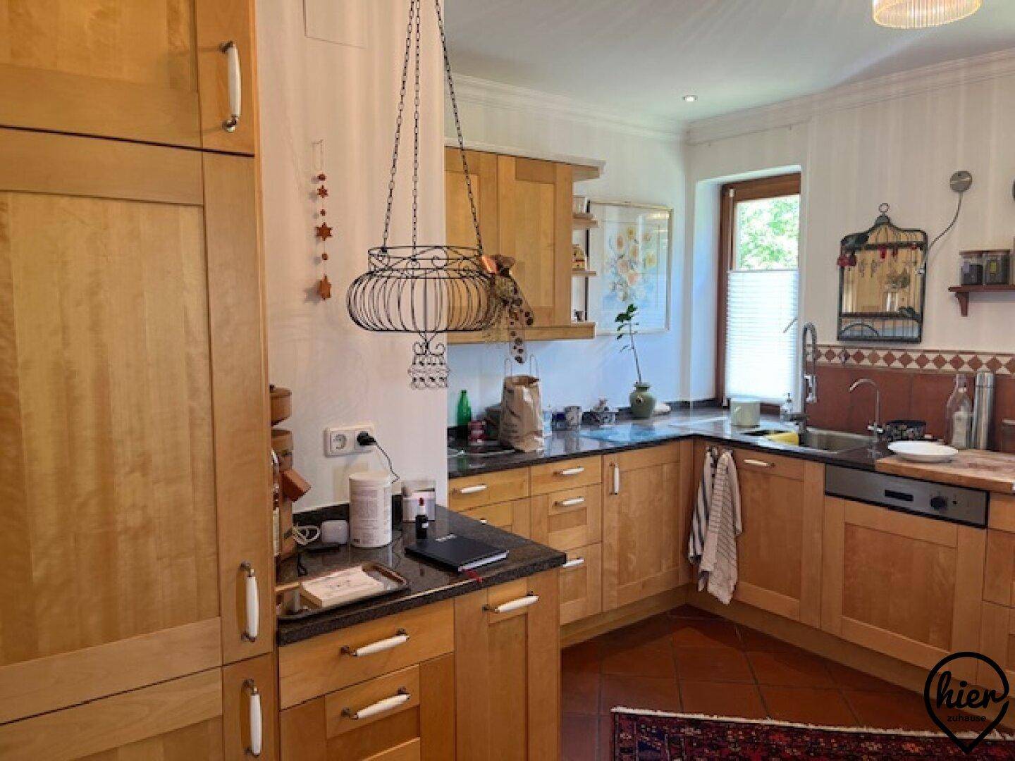 Gemütliche Küche mit Holzschränken, dunklen Arbeitsplatten und Terrakotta-Fliesenboden.