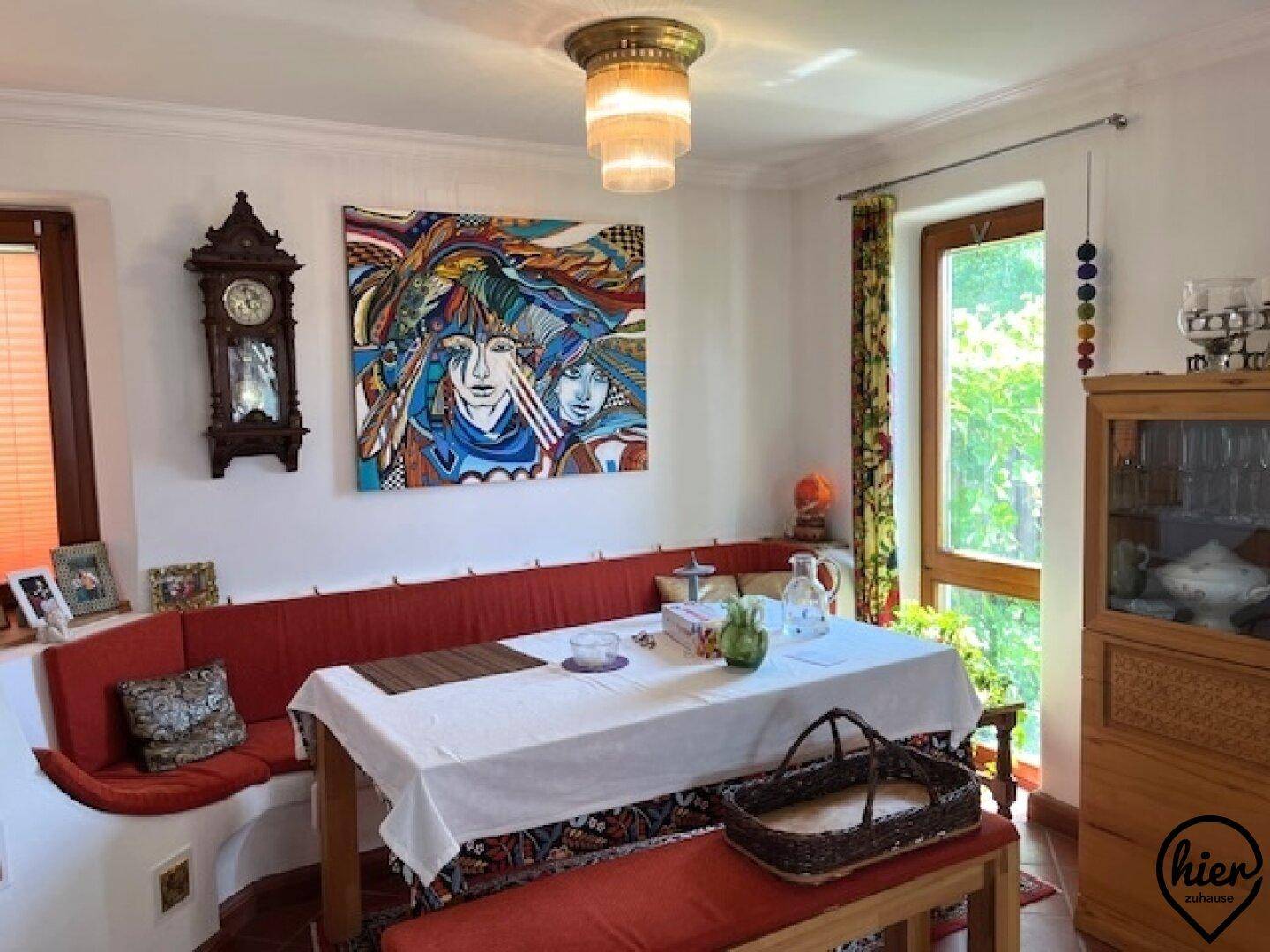 Heller Essbereich mit großem Tisch, Sitzbänken und einem Schrank, umgeben von Fenstern.