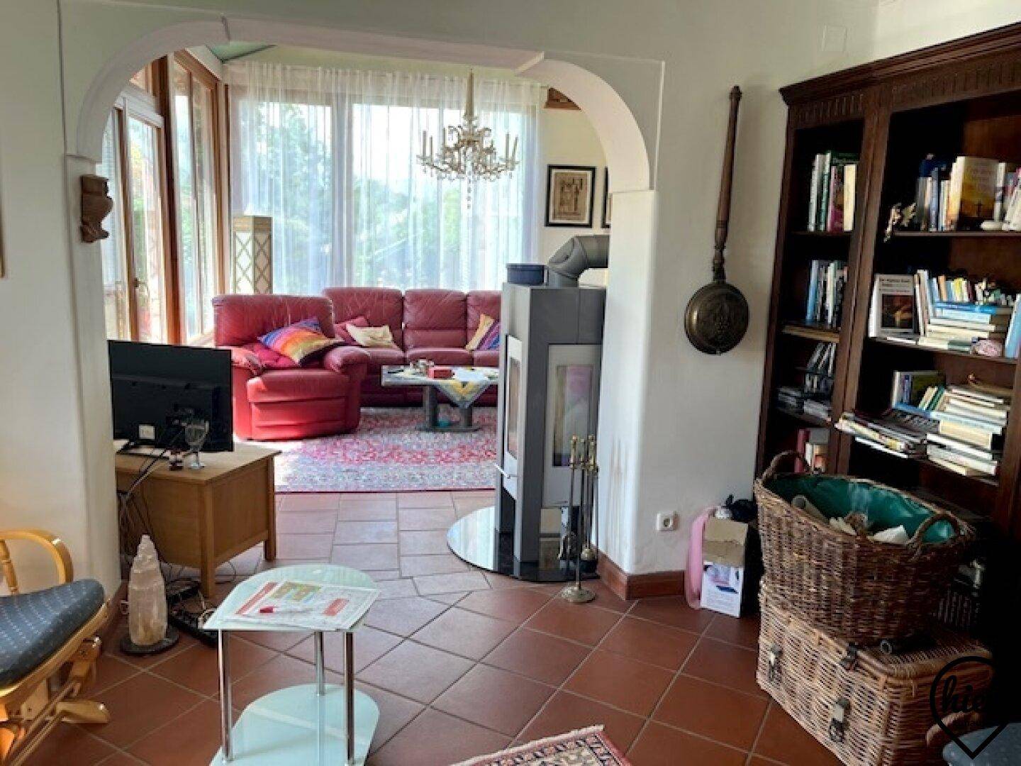 Gemütliches Wohnzimmer mit roten Ledersofas, modernem Holzofen und Zugang zu einem Wintergarten.