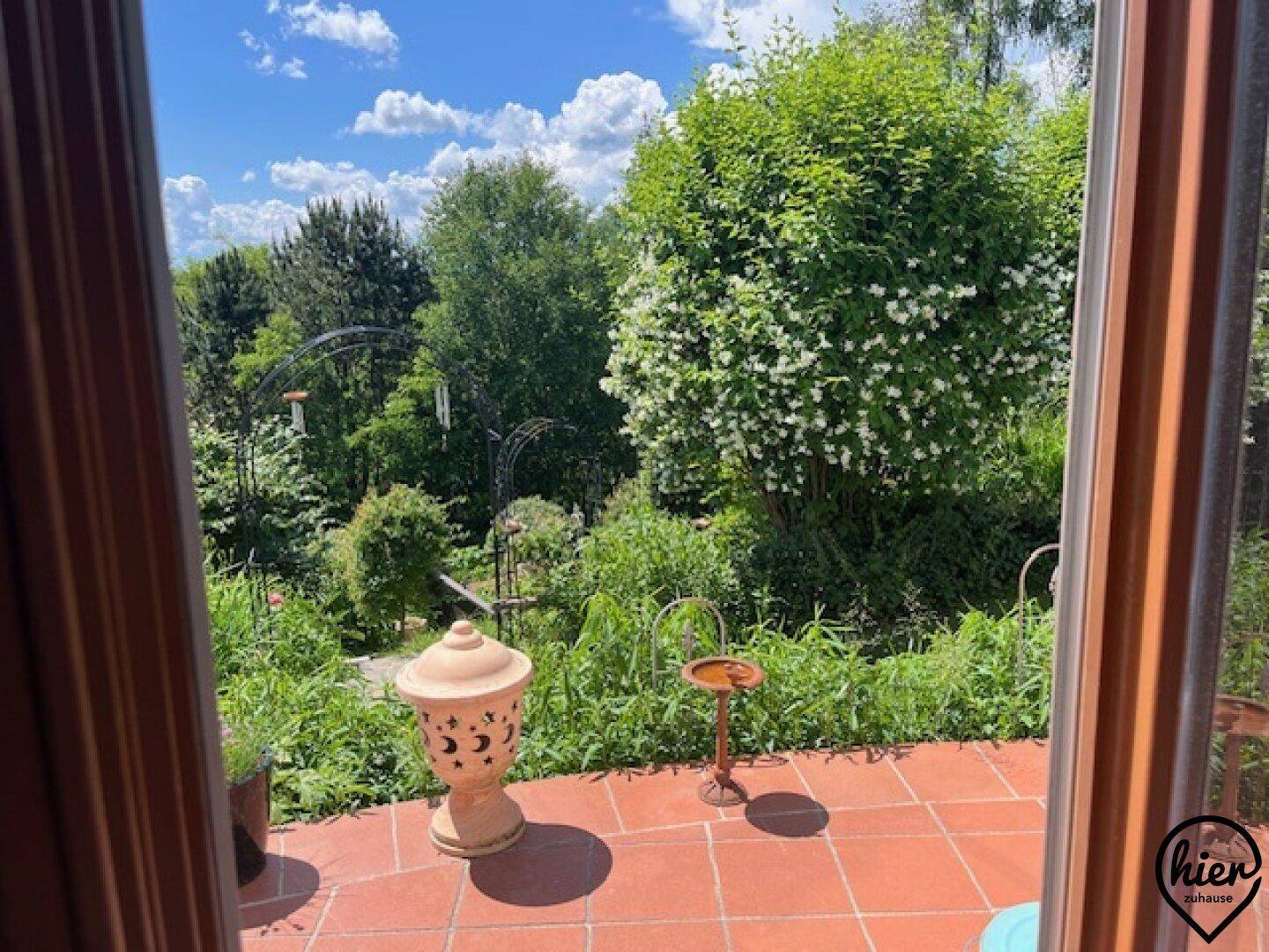 Blick von innen auf eine geflieste Terrasse mit Gartendekoration und üppigem Grün.