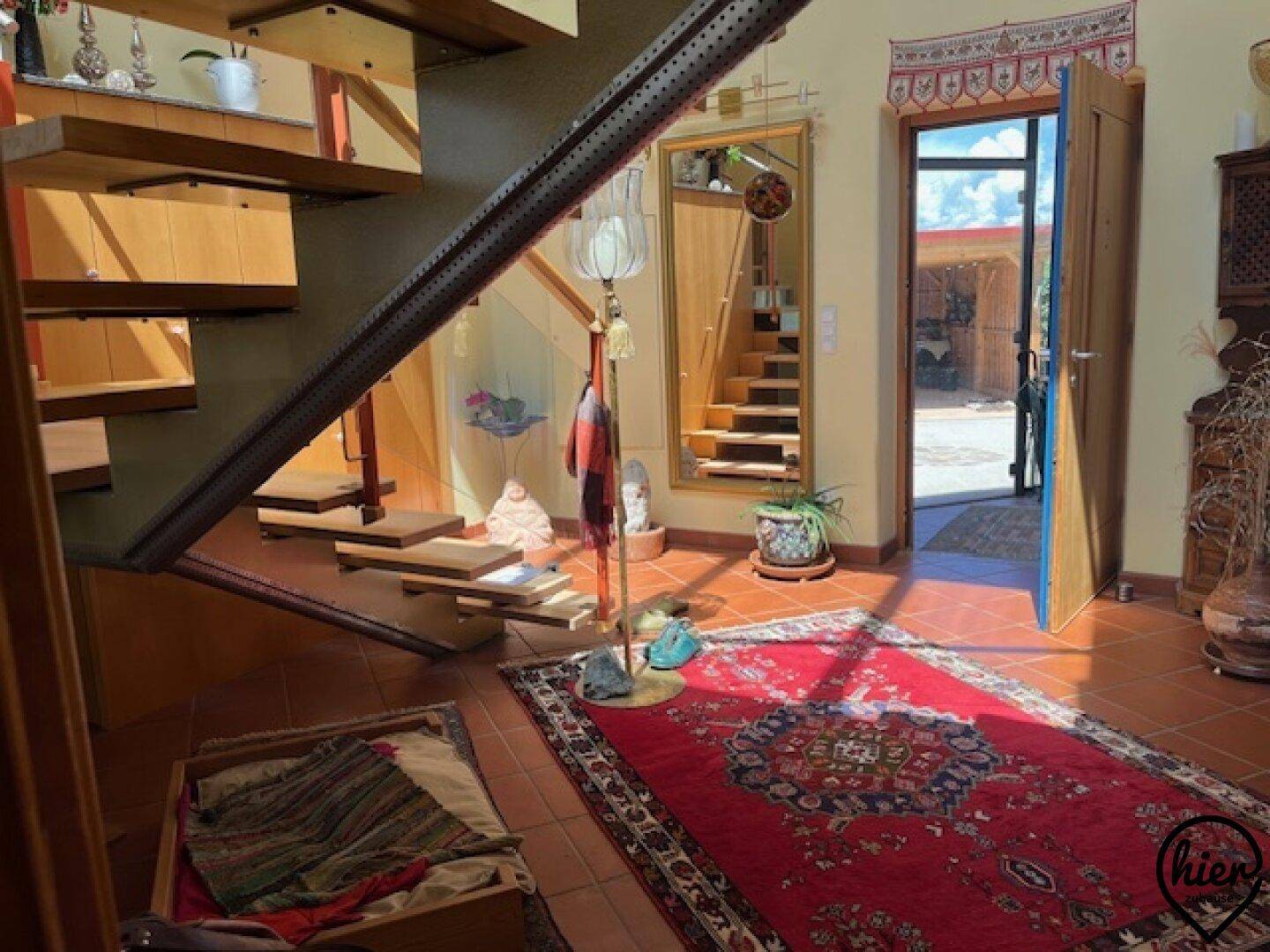 Geräumiger Flur mit rotem Teppich, Terrakotta-Fliesen und offener Holztreppe zum Obergeschoss.