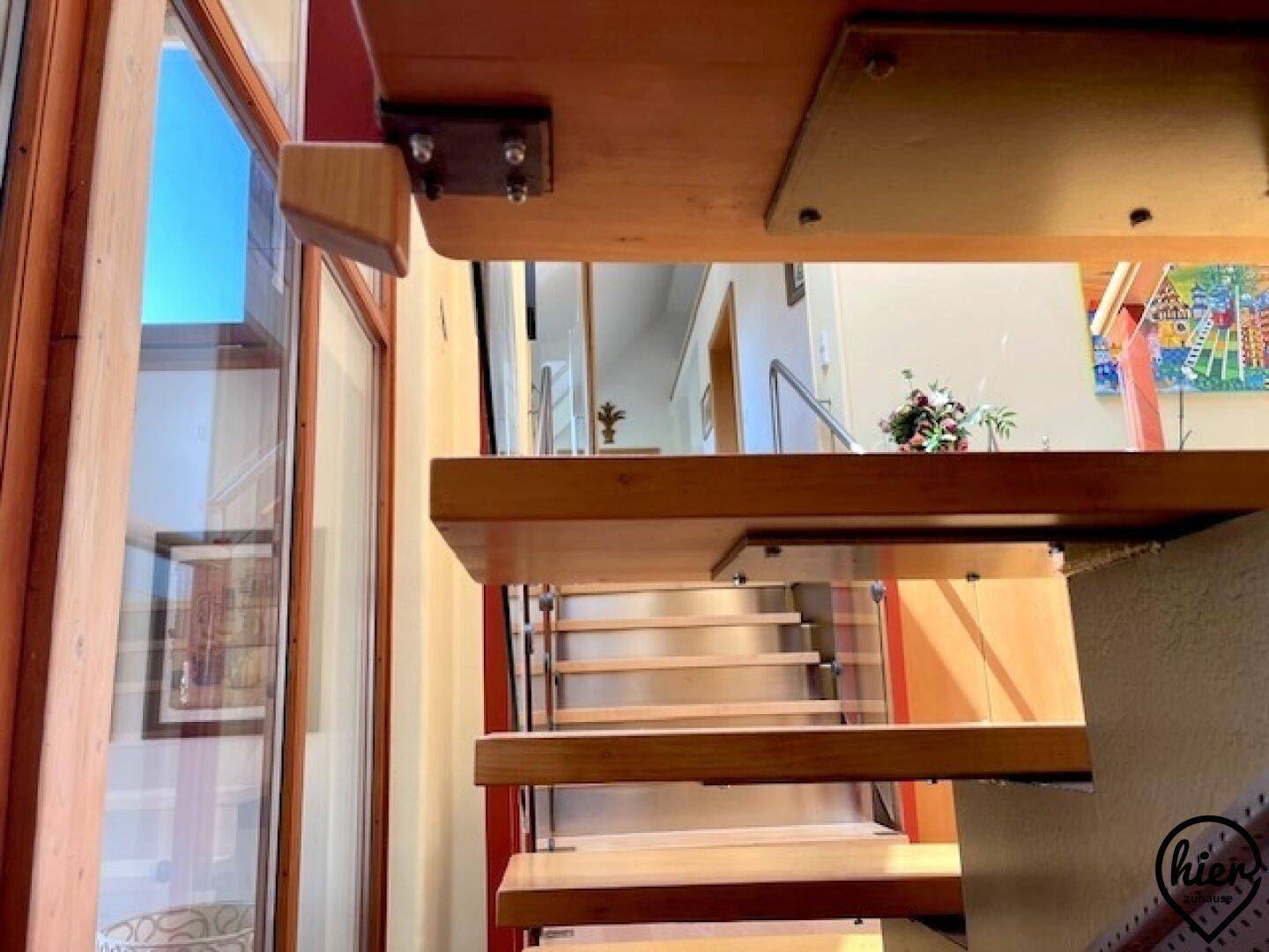 Detailansicht der Holztreppe mit Glasgeländer, die das offene Raumkonzept betont.