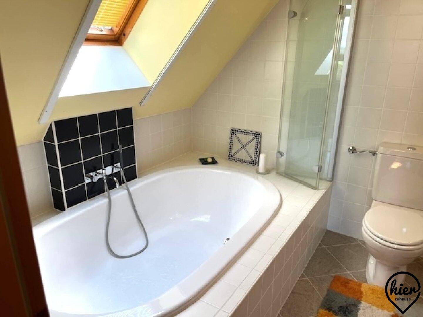 Badezimmer im Dachgeschoss mit Badewanne, Dusche, Toilette und einem Dachfenster für Tageslicht.