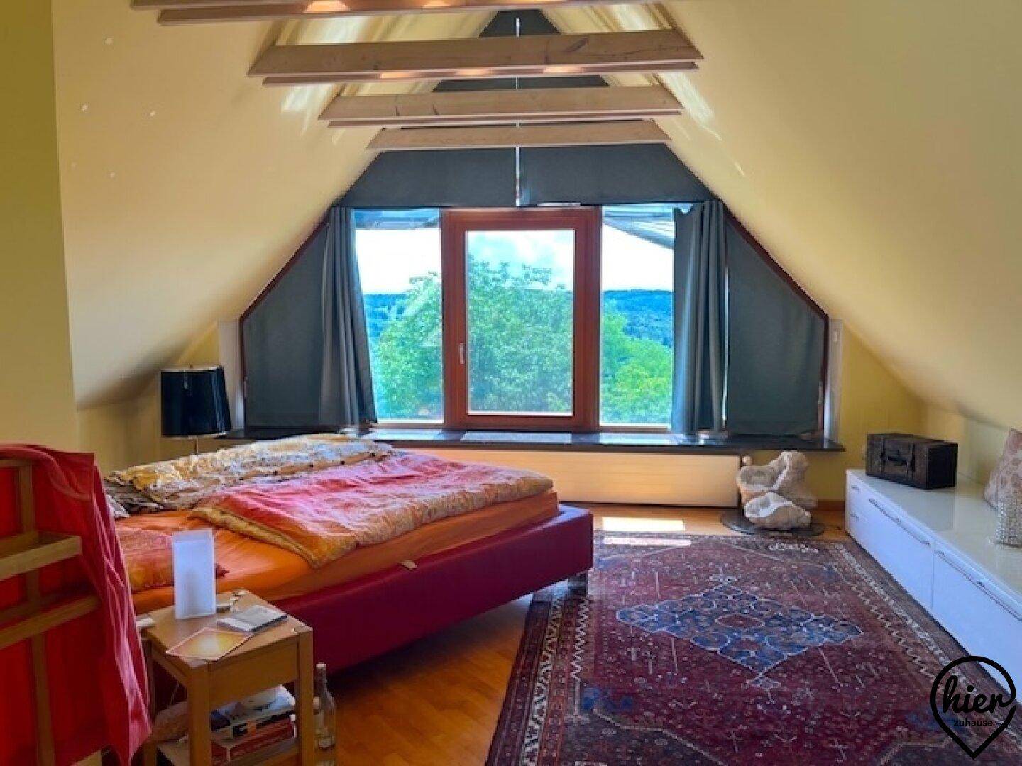 Gemütliches Schlafzimmer im Dachgeschoss mit großem Fenster, Holzboden und weitem Ausblick.