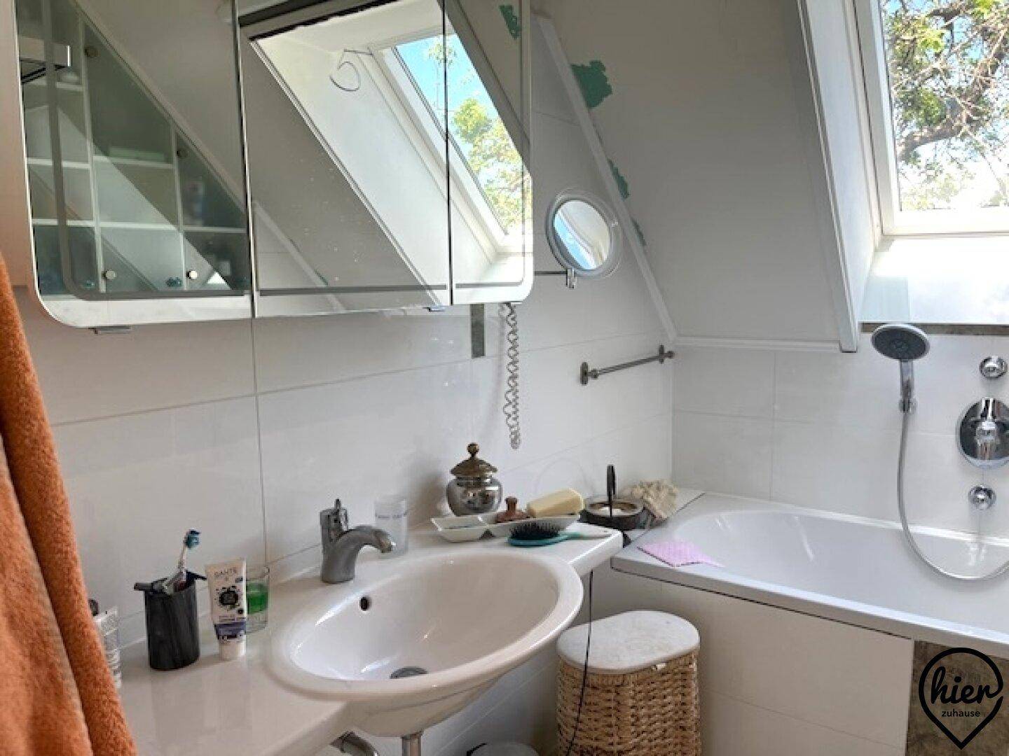 Helles Badezimmer mit Badewanne, Waschbecken und Dachfenster unter einer Dachschräge.