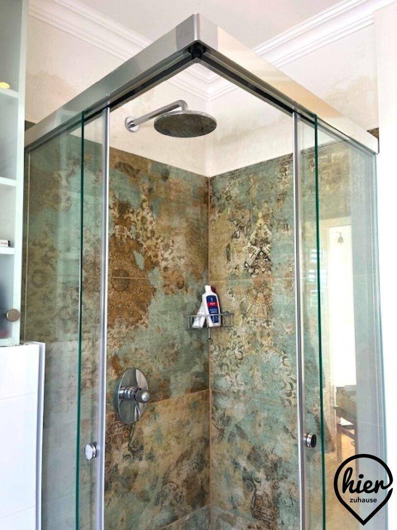 Moderne Duschkabine mit gemusterten Fliesen und einer Regendusche.