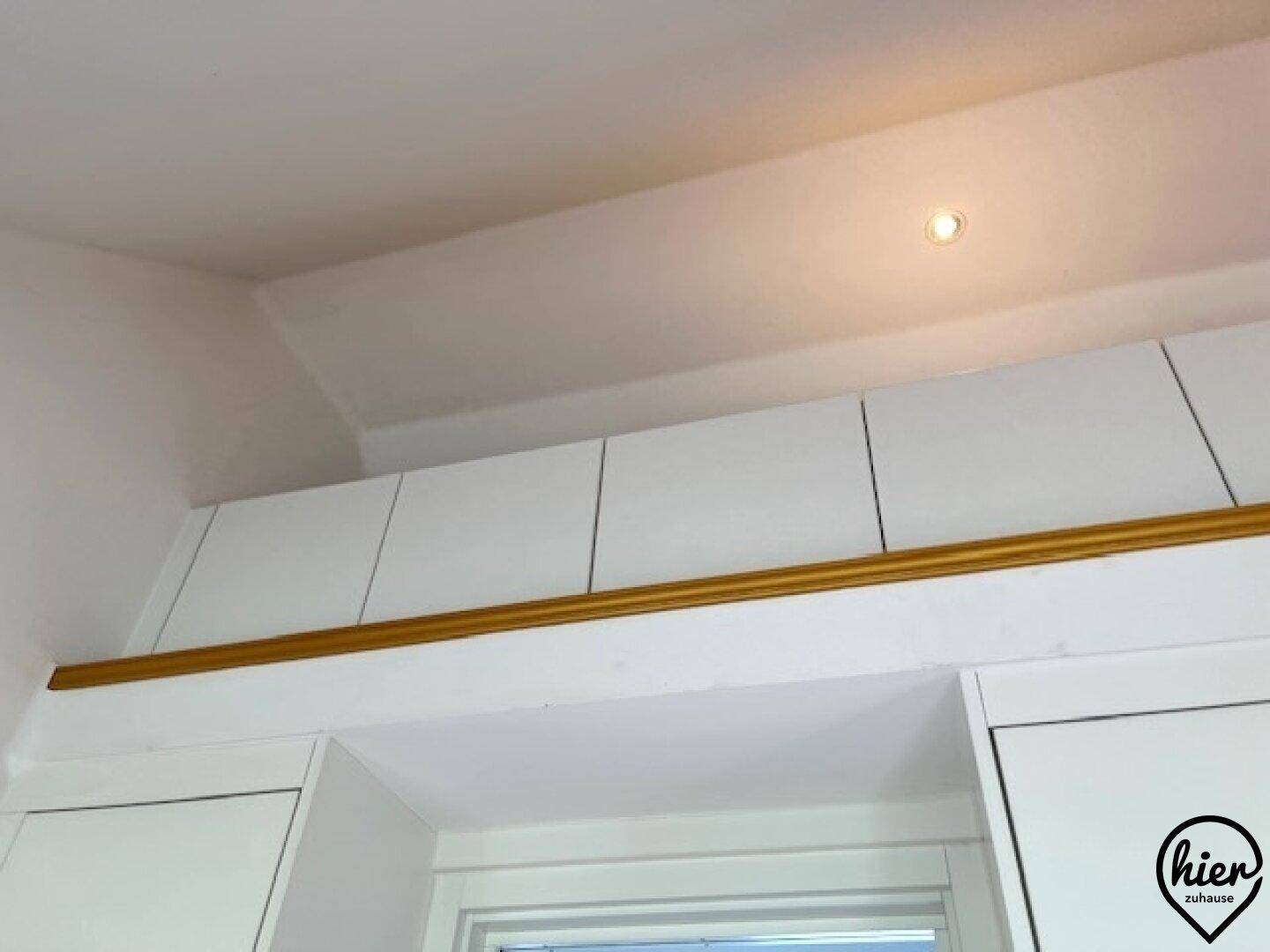 Weiße Oberschränke mit goldener Zierleiste und integrierter Beleuchtung.