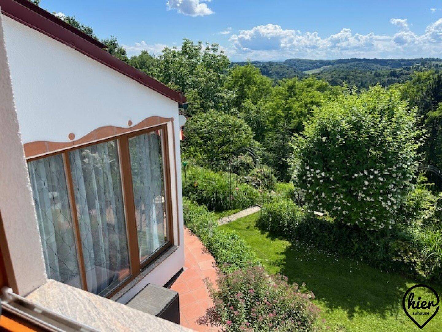Blick von einem Balkon auf einen gepflegten Garten und die weite grüne Landschaft.
