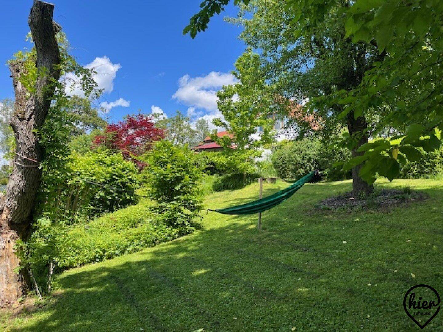 Entspannender Gartenbereich mit einer Hängematte zwischen Bäumen an einem sonnigen Tag.
