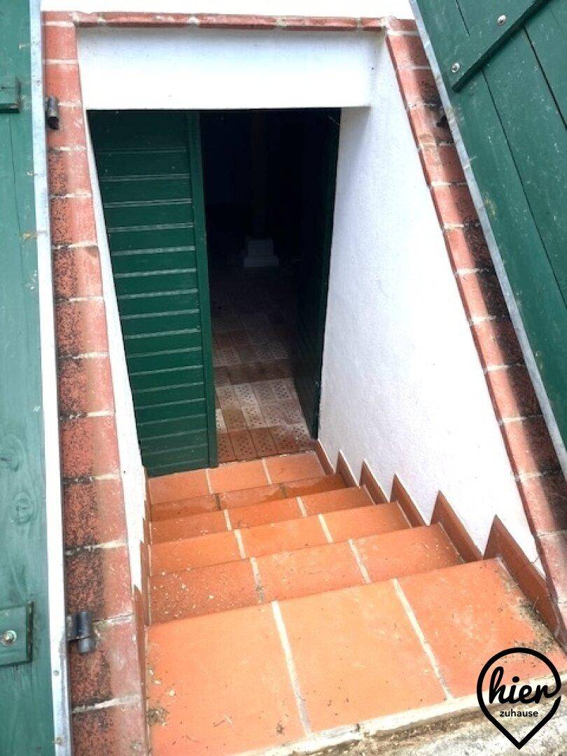 Außentreppe führt hinunter zum Kellereingang mit Terrakotta-Fliesen und grünen Fensterläden.