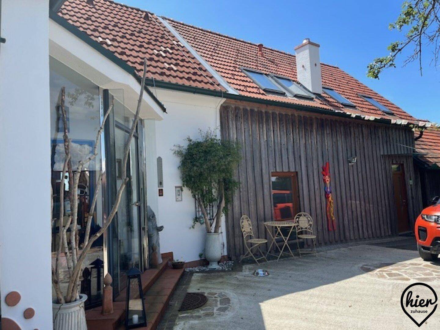 Hausfassade mit traditionellem Ziegeldach, moderner Holzverkleidung und kleinem Eingangsbereich mit Sitzgelegenheit.