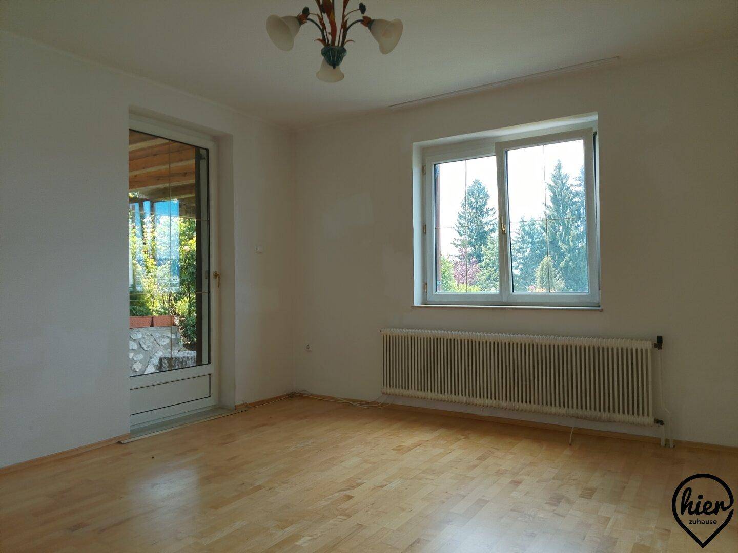 Heller Raum mit Parkettboden, großem Fenster und Zugang zu einer Terrasse oder Loggia.