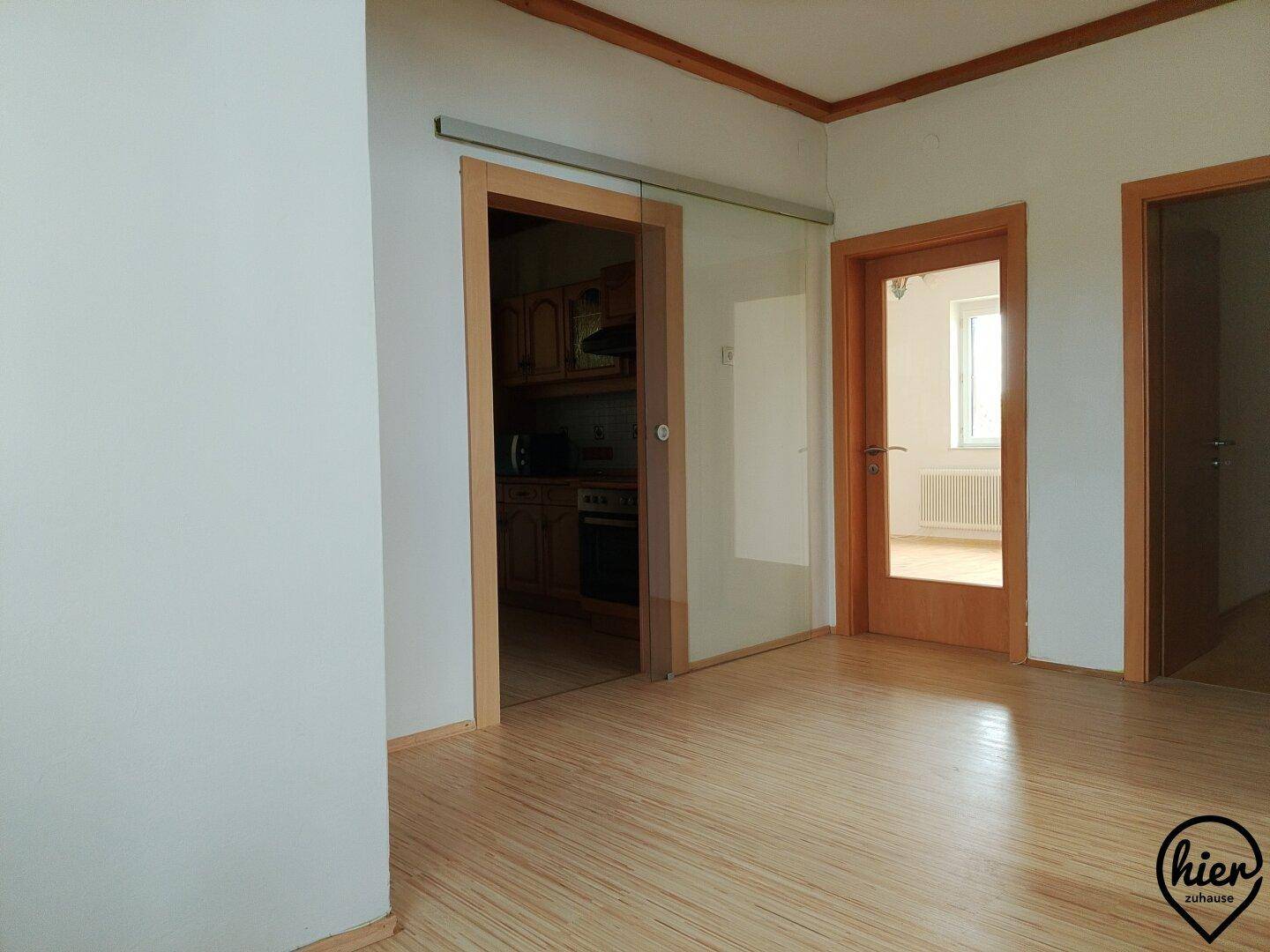 Heller Flur mit Holzboden und Glasschiebetür, die zu einem weiteren Raum führt.
