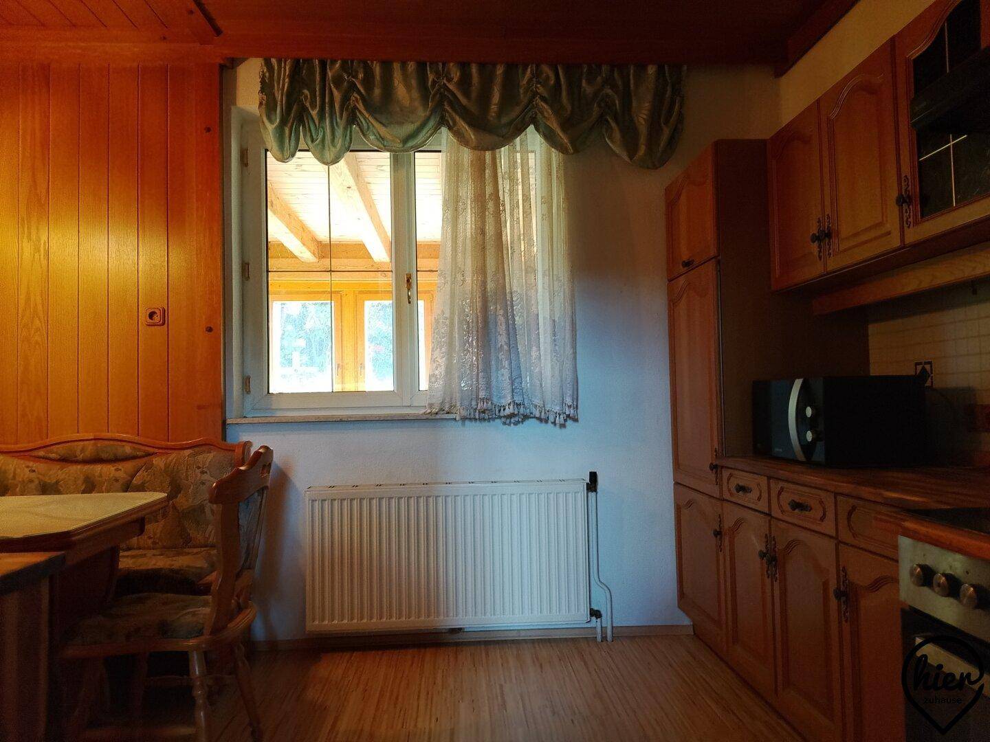 Traditionelle Küche mit Holzschränken, Essbereich und Fenster mit Vorhang.