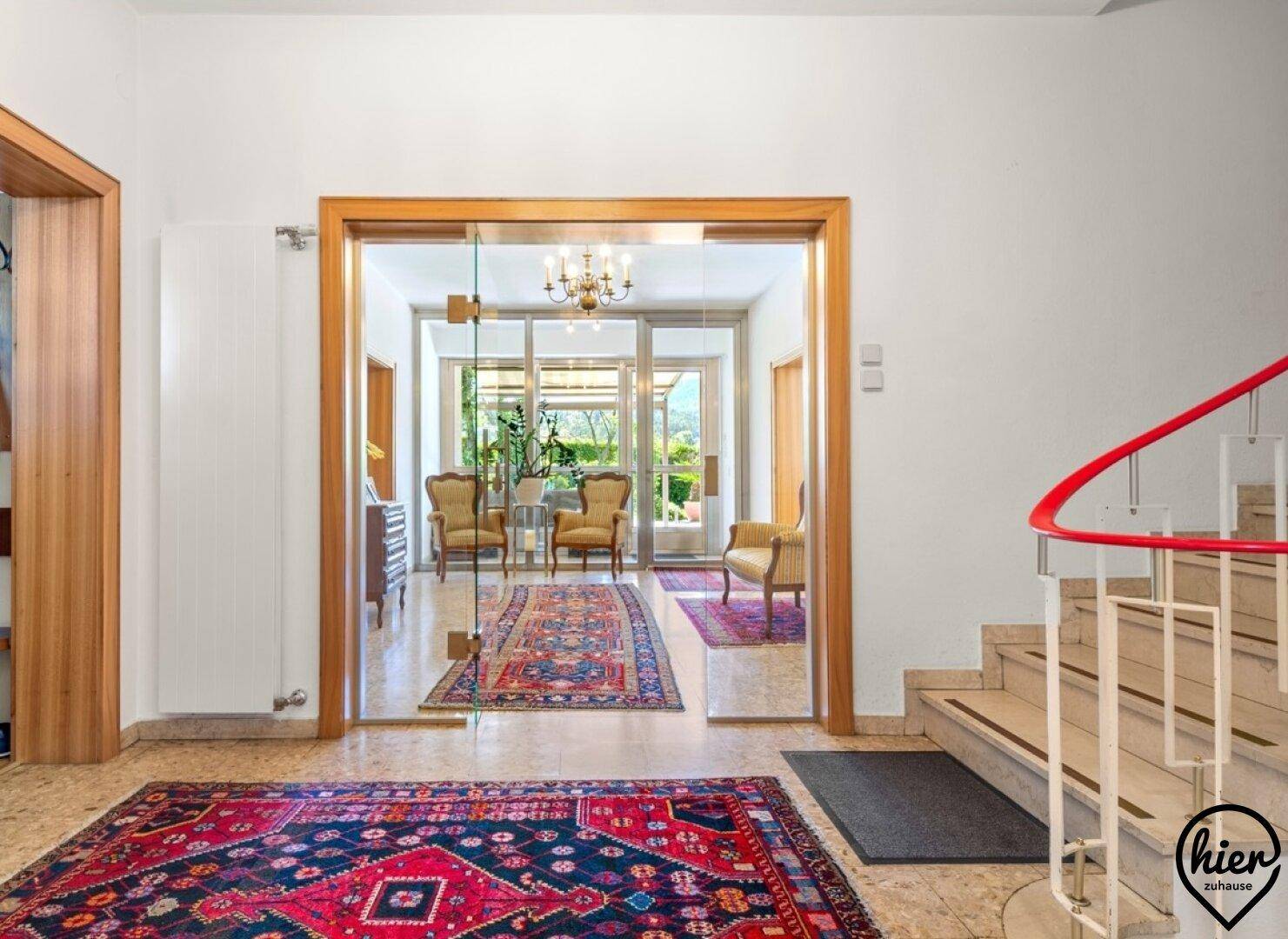 Heller Eingangsbereich mit Marmorboden, eleganten Teppichen und einer geschwungenen Treppe, die in den Wohnbereich führt.