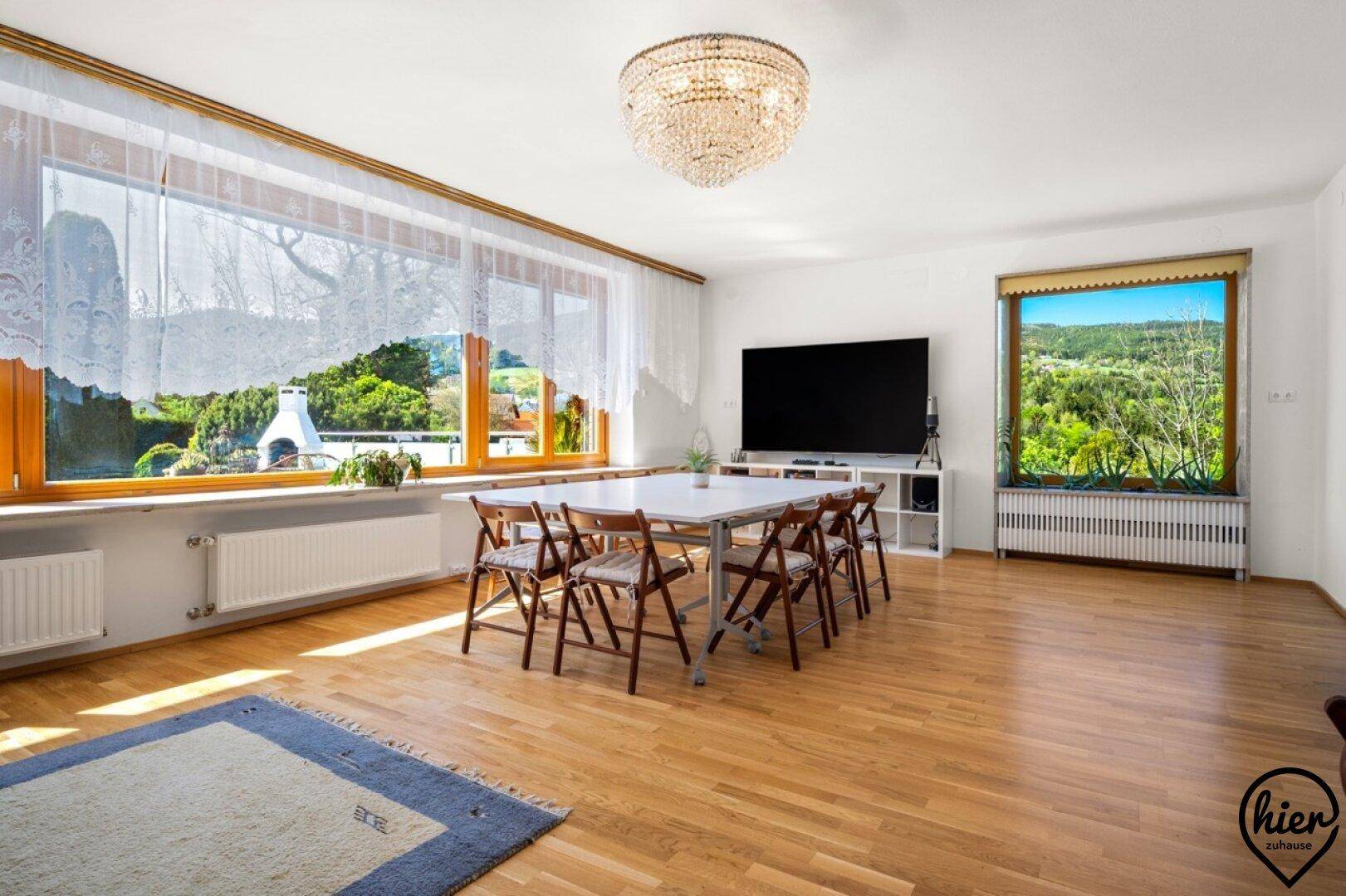 Geräumiges Wohnzimmer mit Holzboden, großzügigen Fenstern und einem großen Esstisch, ideal für Familienessen.