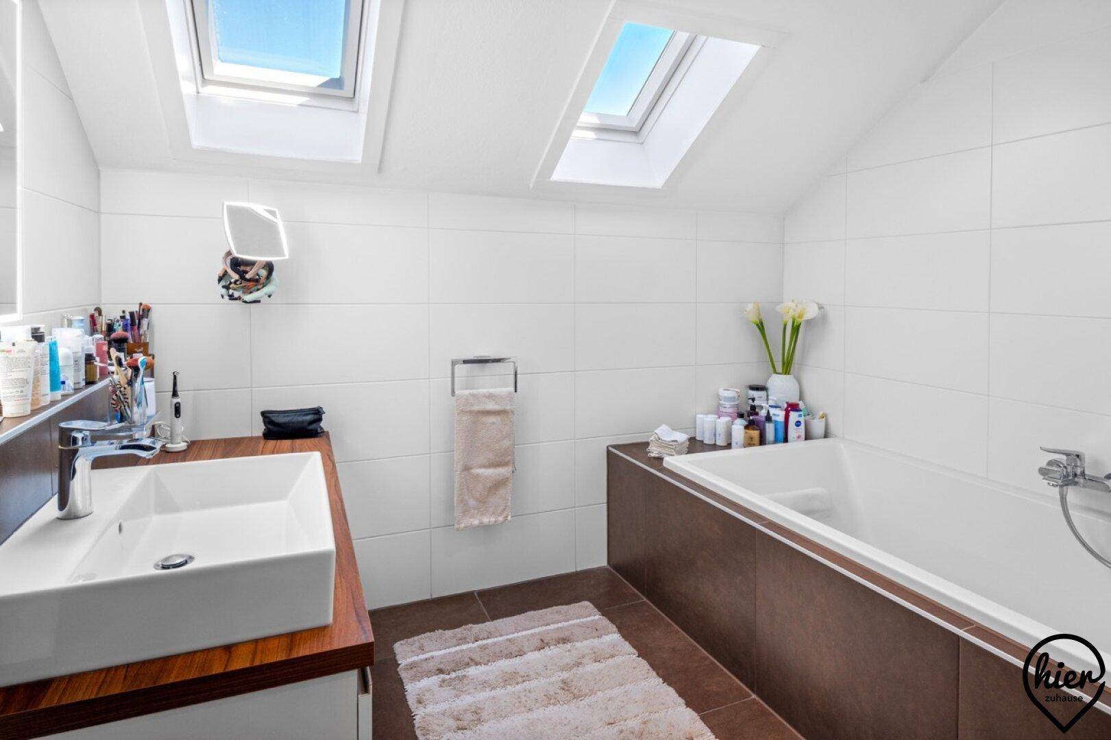 Modernes Badezimmer im Dachgeschoss mit Badewanne, Einzelwaschbecken und zwei Dachfenstern, sehr hell.