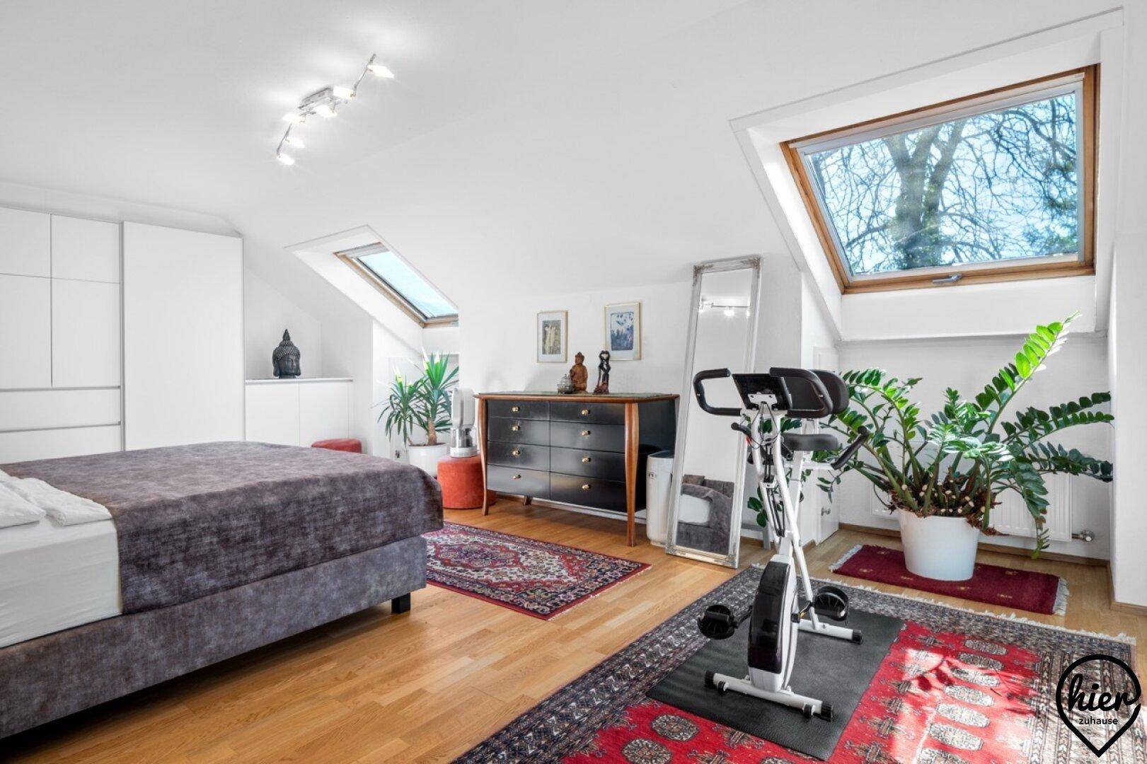 Helles Schlafzimmer im Dachgeschoss mit Holzboden, Dachfenstern und Fitnessgerät.