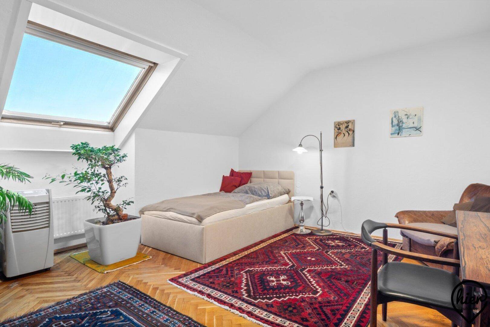Helles Schlafzimmer im Dachgeschoss mit Holzboden, Teppich und großem Dachfenster.