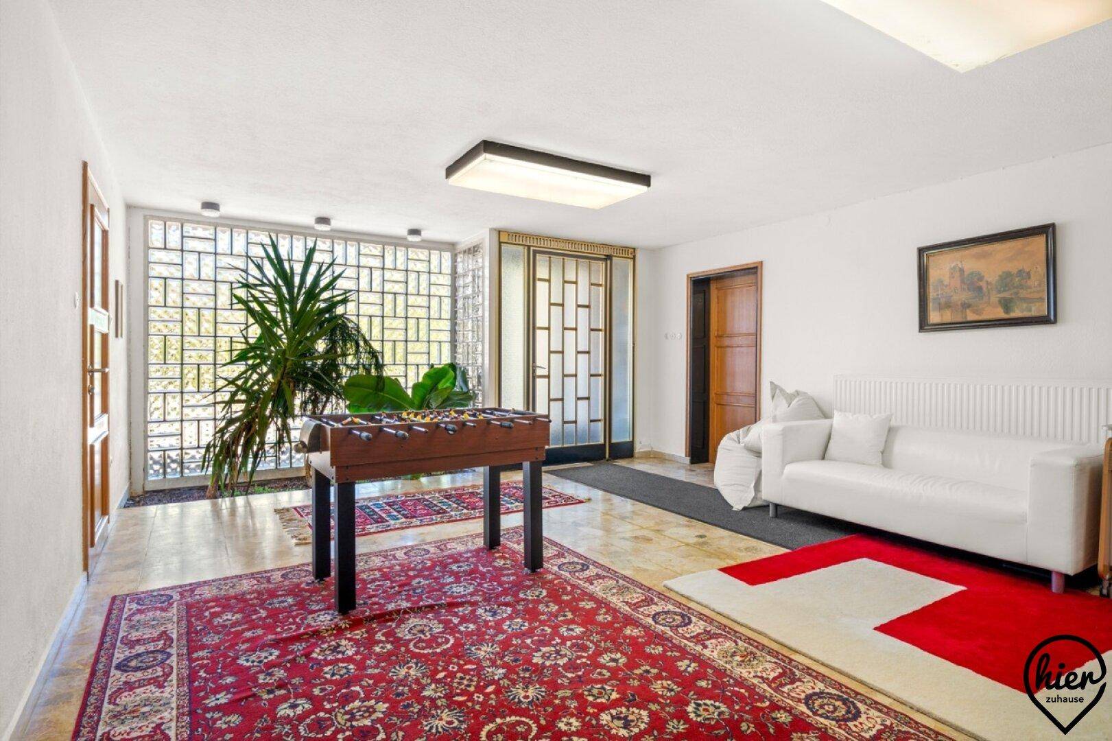 Geräumiger Wohnbereich mit Tischfußball, weißem Sofa und großen Fenstern.