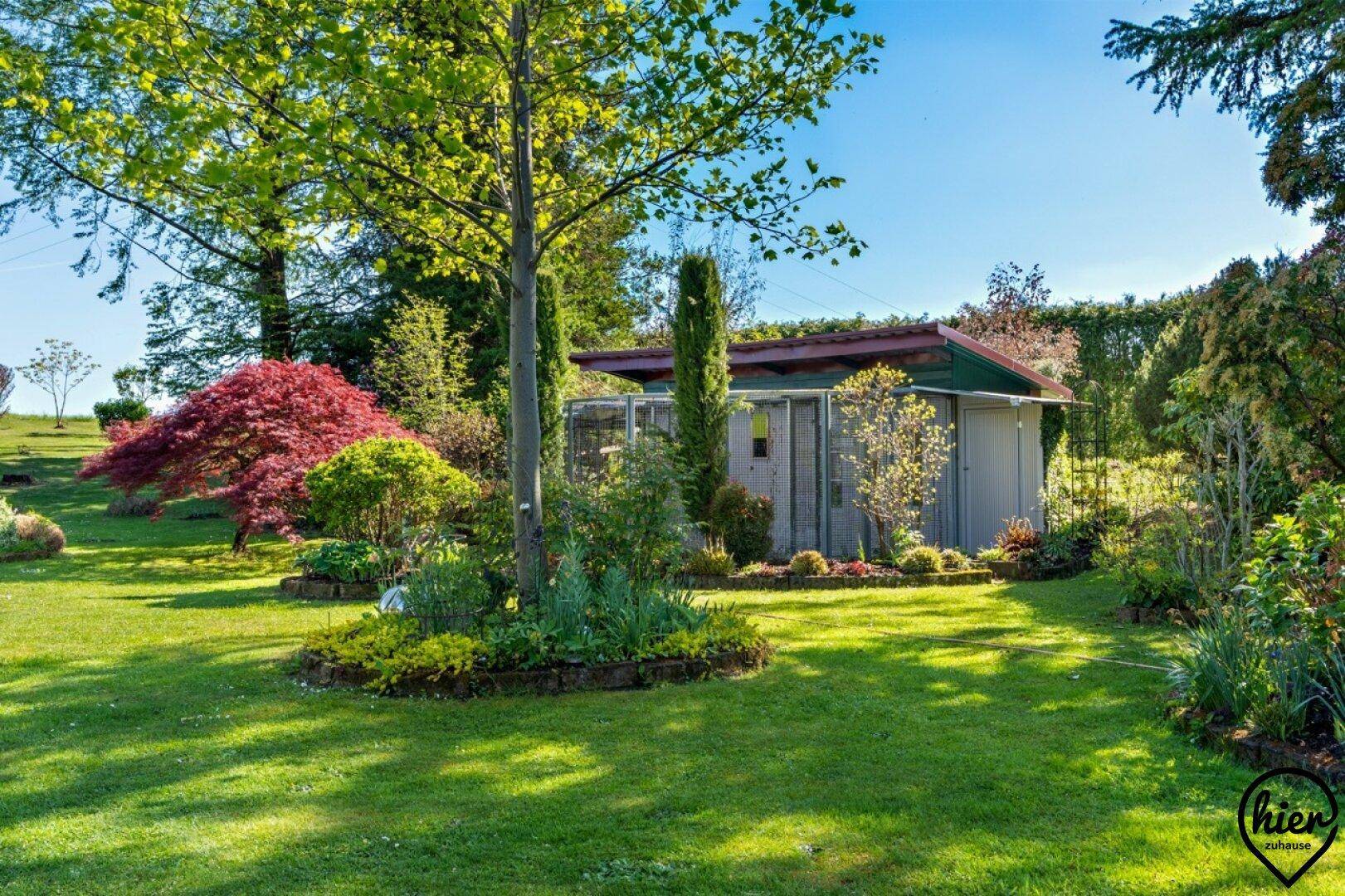 Weitläufiger Garten mit Rasen, Bäumen und einem kleinen Gartenhaus im Hintergrund.