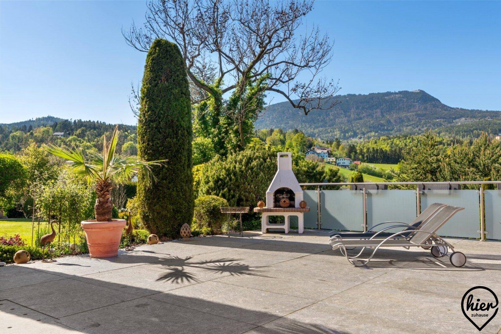 Sonnenterrasse mit Grillplatz, Liegestühlen und weitem Blick auf die umliegende grüne Hügellandschaft.