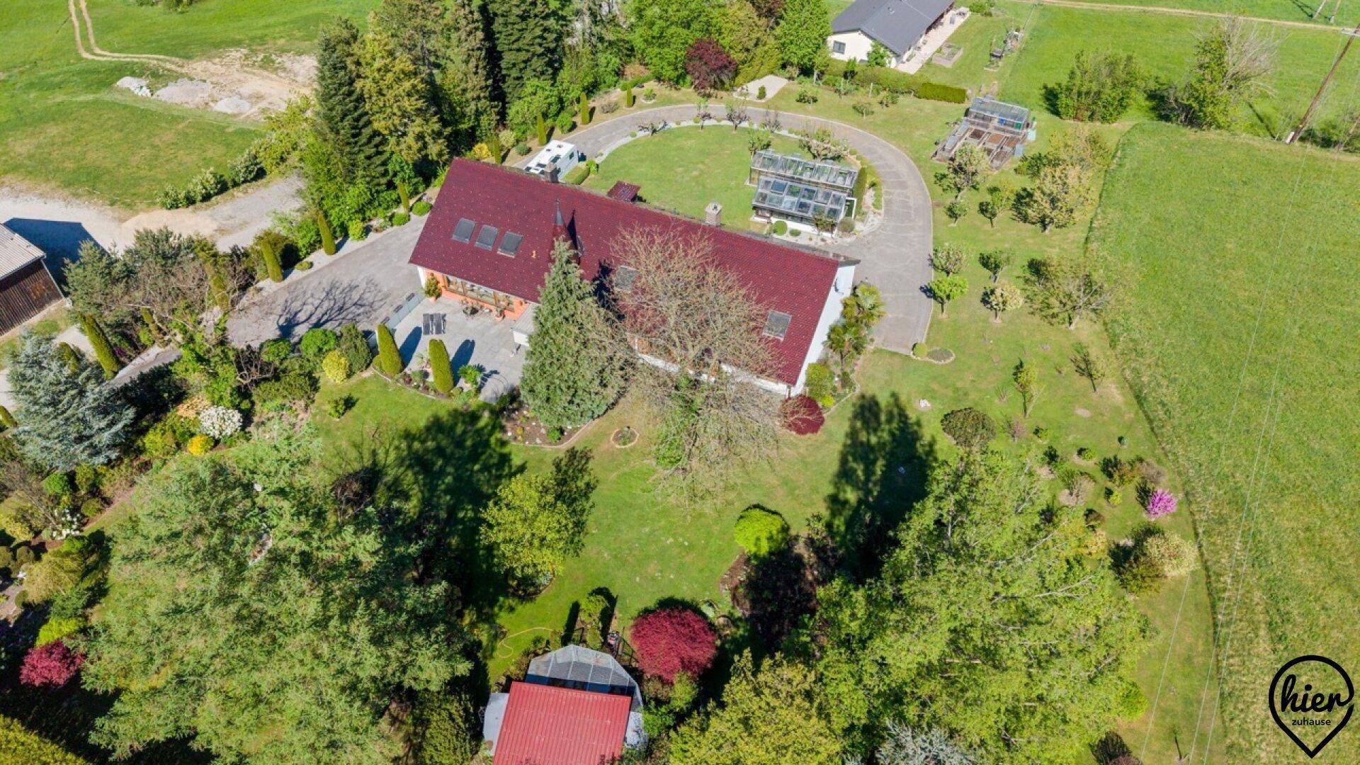 Luftaufnahme eines weitläufigen Anwesens mit Haus, Garten und Gewächshäusern.