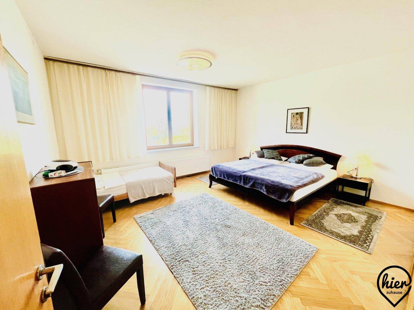 Geräumiges Schlafzimmer mit Fischgrätparkett, einem großen Doppelbett und einem zusätzlichen Einzelbett, hell und einladend.