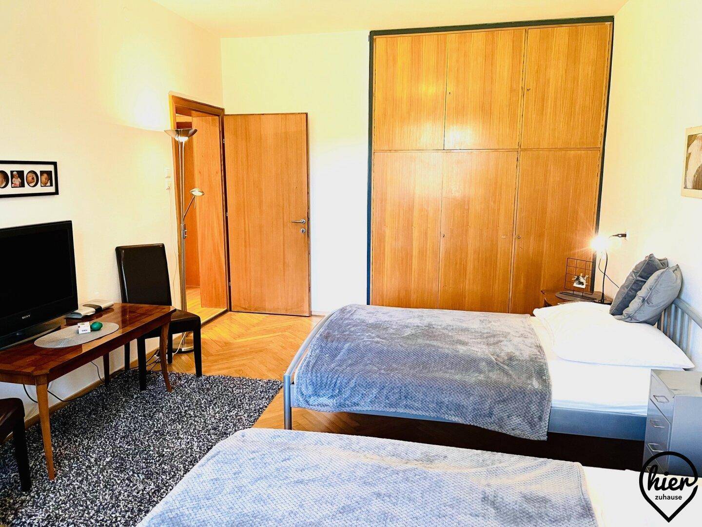 Helles Schlafzimmer mit zwei Einzelbetten, Fischgrätparkett und einem großen Einbauschrank, praktisch und funktional.
