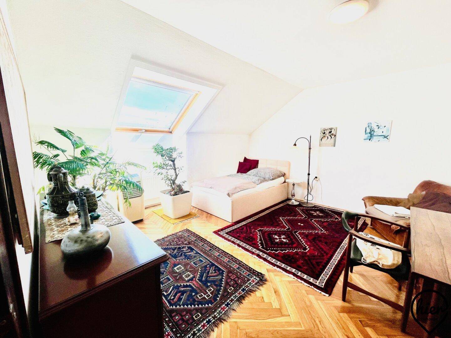 Gemütliches Schlafzimmer im Dachgeschoss mit Holzboden, Teppichen und Dachfenster.