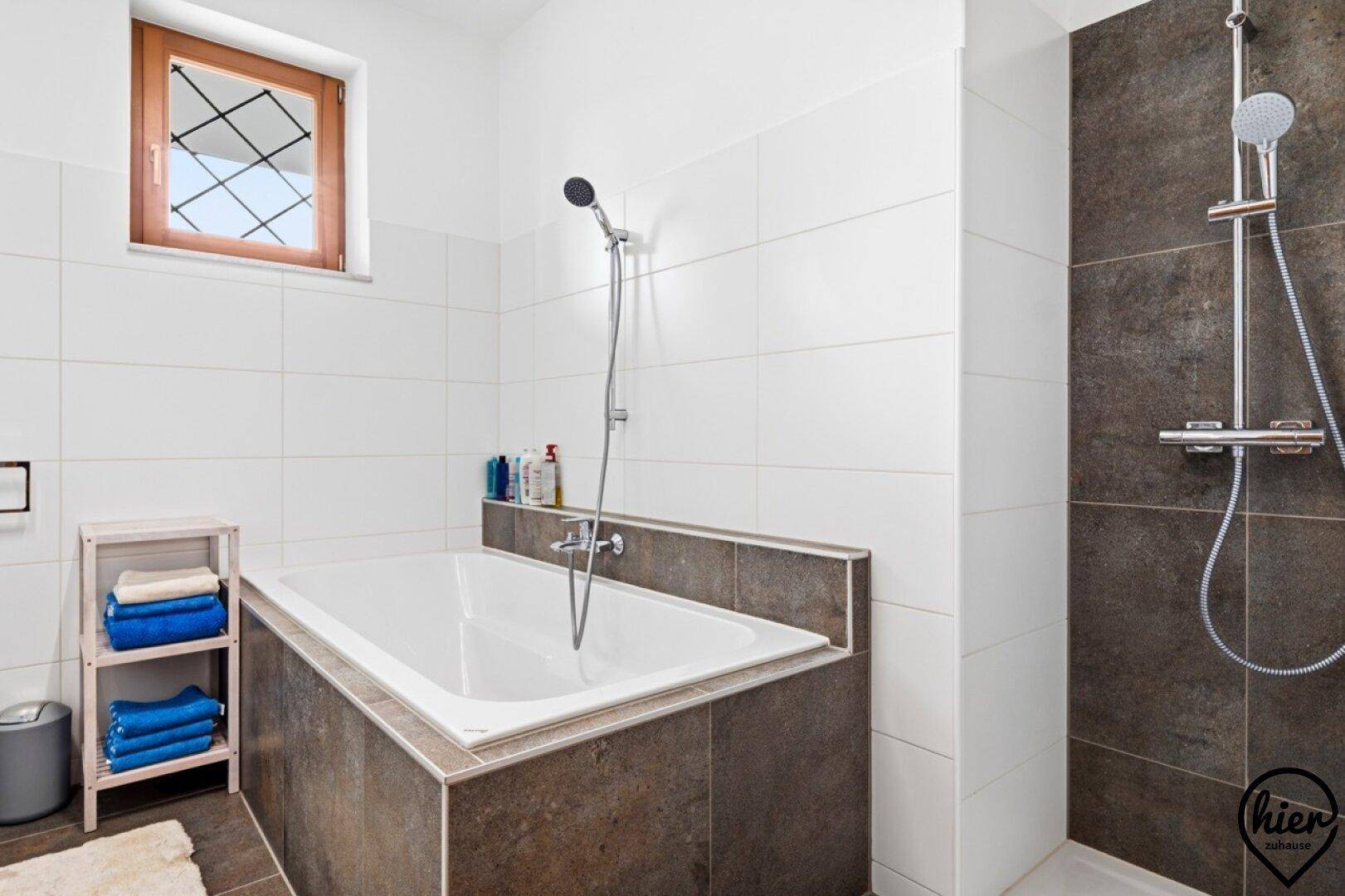 Helles Badezimmer mit Badewanne und separater Dusche, ausgestattet mit weißen und braunen Fliesen.