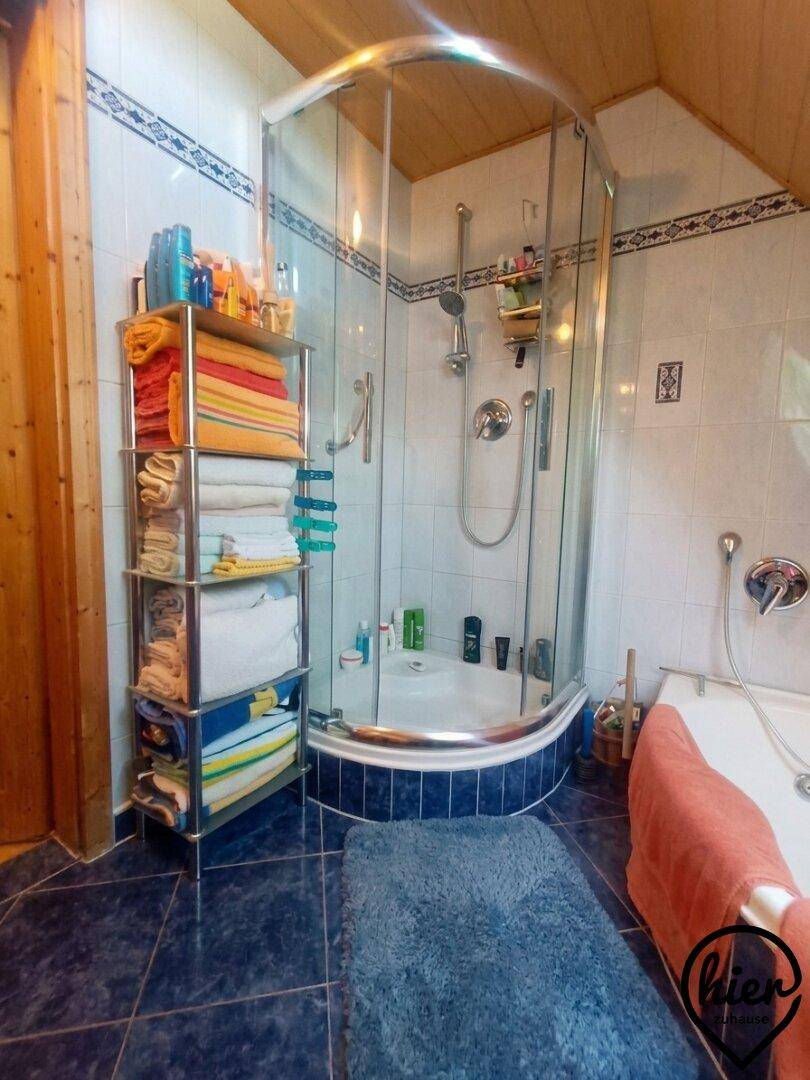 Badezimmer mit Duschkabine, Badewanne und blauen Fliesen im Dachgeschoss mit Dachschräge.