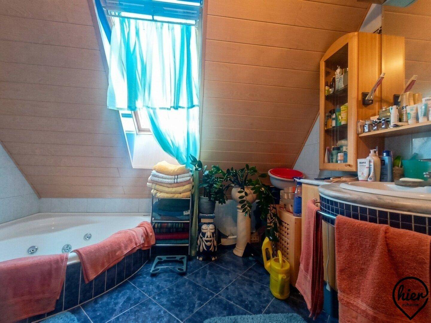 Badezimmer mit Eckbadewanne, Dachfenster und Holzverkleidung im Dachgeschoss.