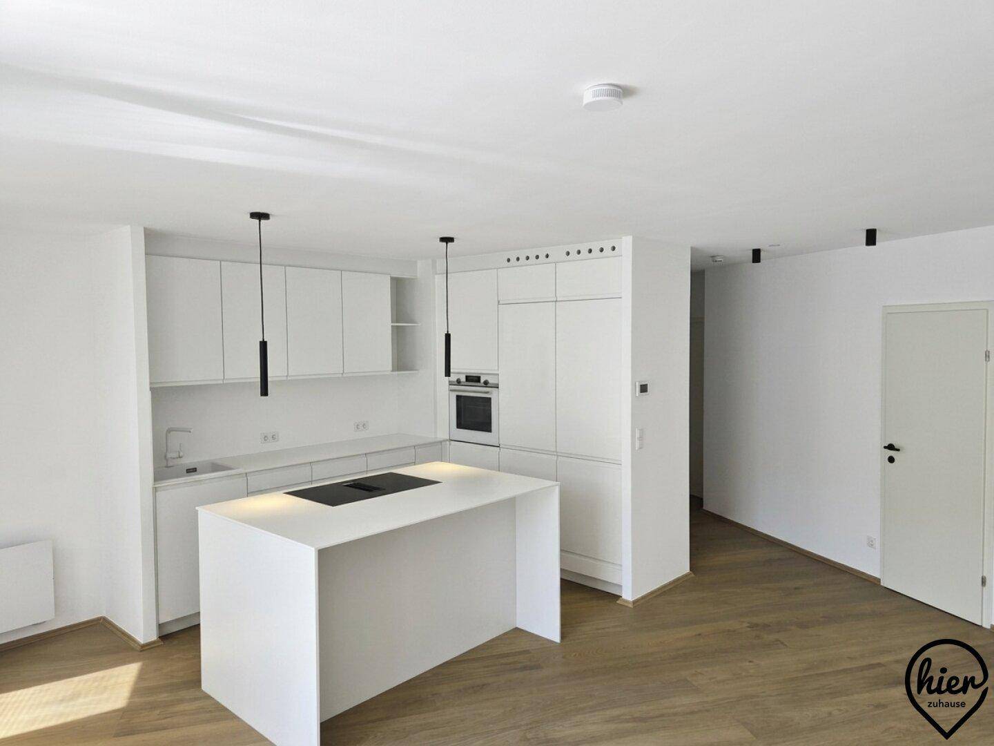 Moderne, offene Küche mit weißer Kücheninsel, integriertem Kochfeld und Einbaugeräten.
