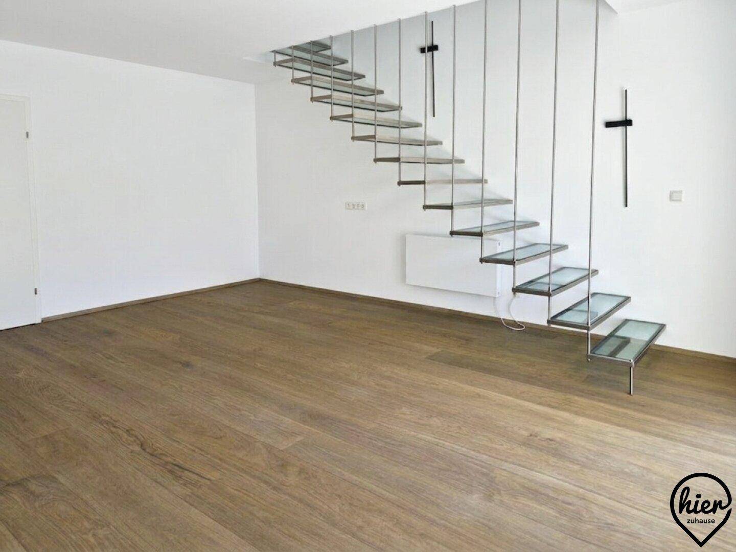 Geräumiges Wohnzimmer mit Holzboden und moderner schwebender Treppe als Blickfang.