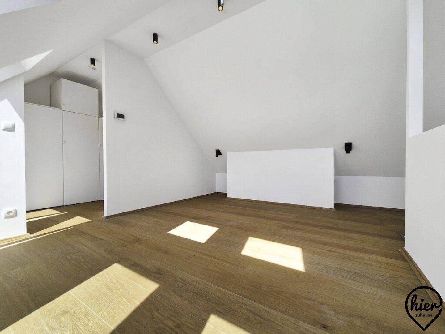 Geräumiges Dachgeschoss mit schrägen Wänden, Holzboden und modernen Deckenleuchten.