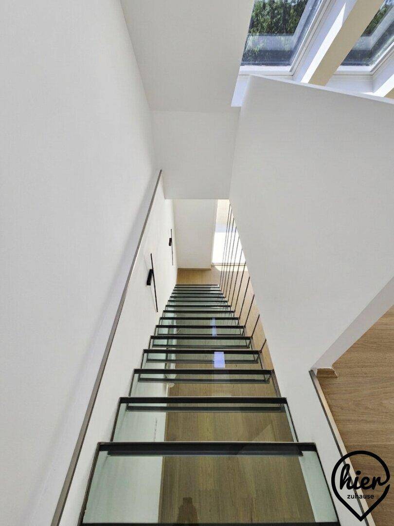 Moderne Treppe mit Glasstufen und Metallgeländer, die viel Licht durchlässt.