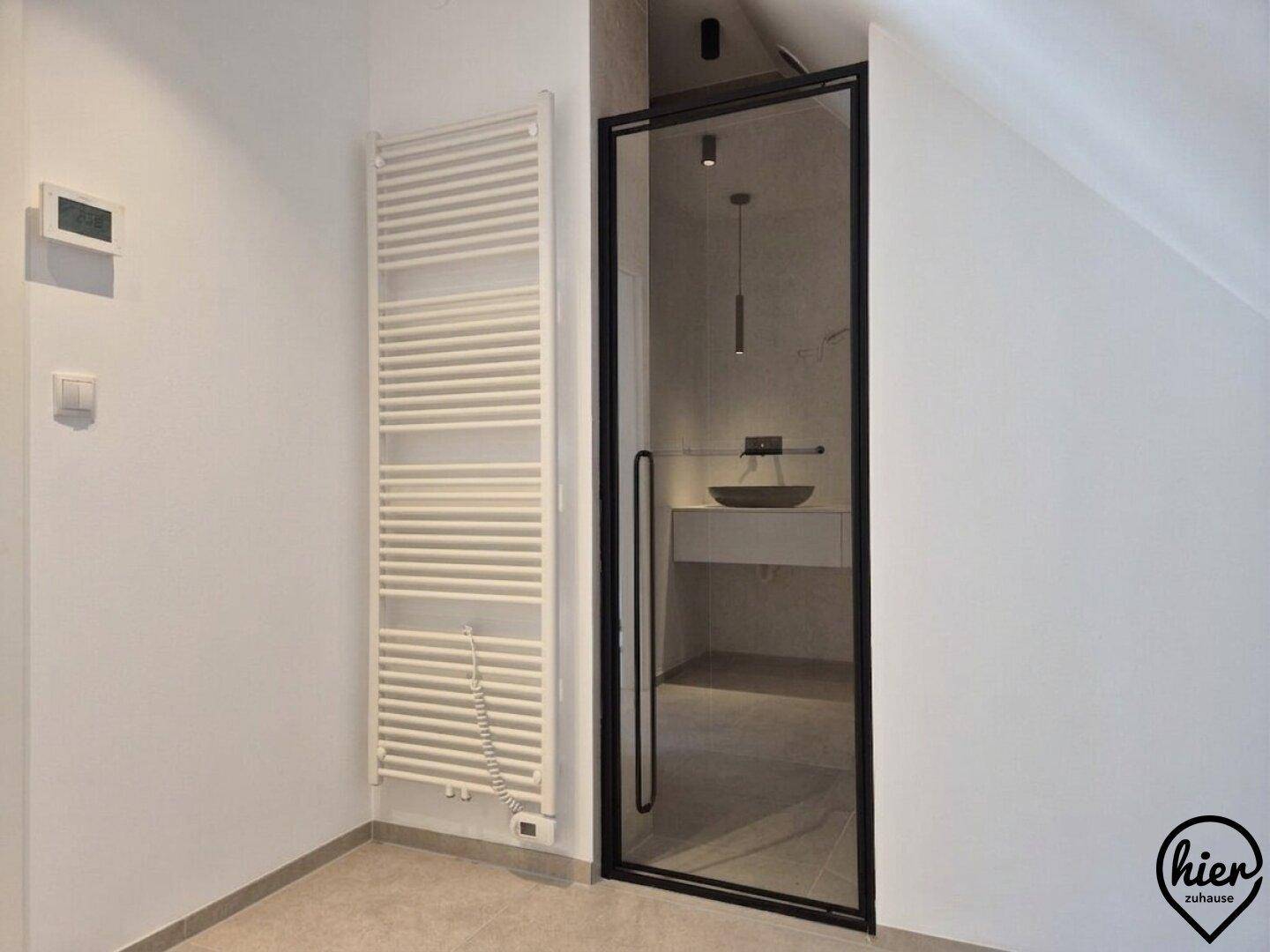 Modernes Badezimmer mit beheiztem Handtuchhalter und Duschkabine mit schwarzem Rahmen.