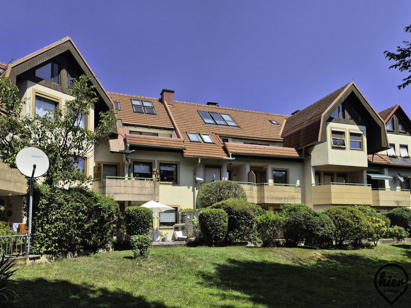 Mehrfamilienhaus mit Satteldach, Balkonen und gepflegter Grünanlage im Vordergrund.
