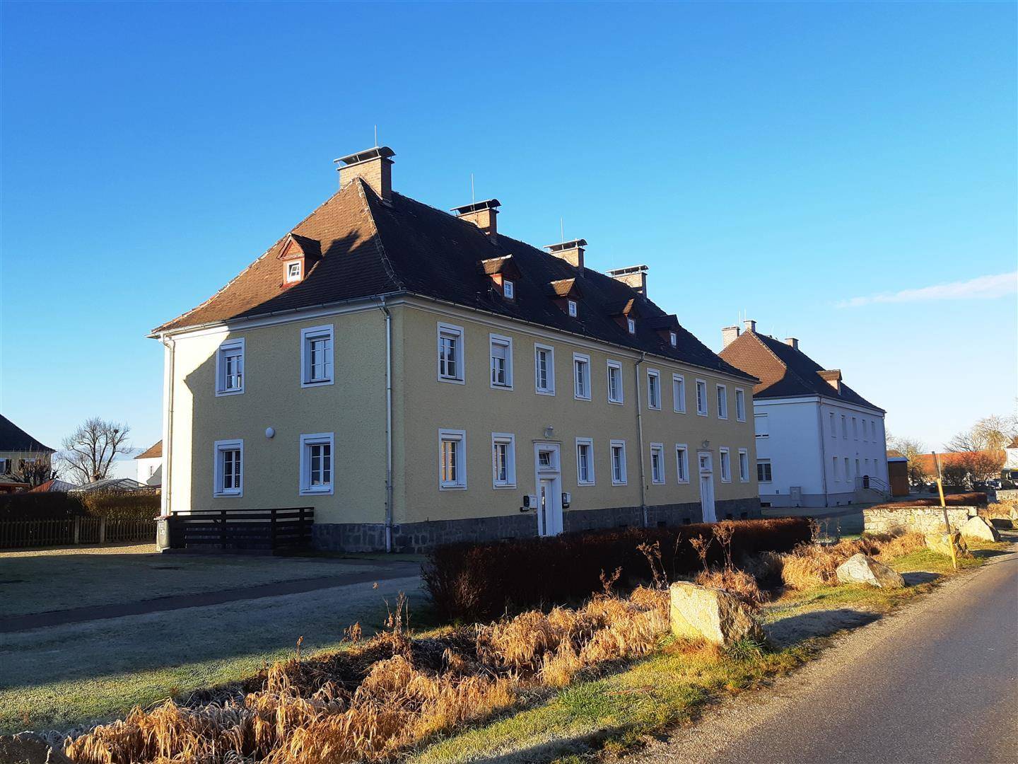 Historisches Gebäude mit gelber Fassade, Mansarddach und vielen Fenstern unter blauem Himmel.