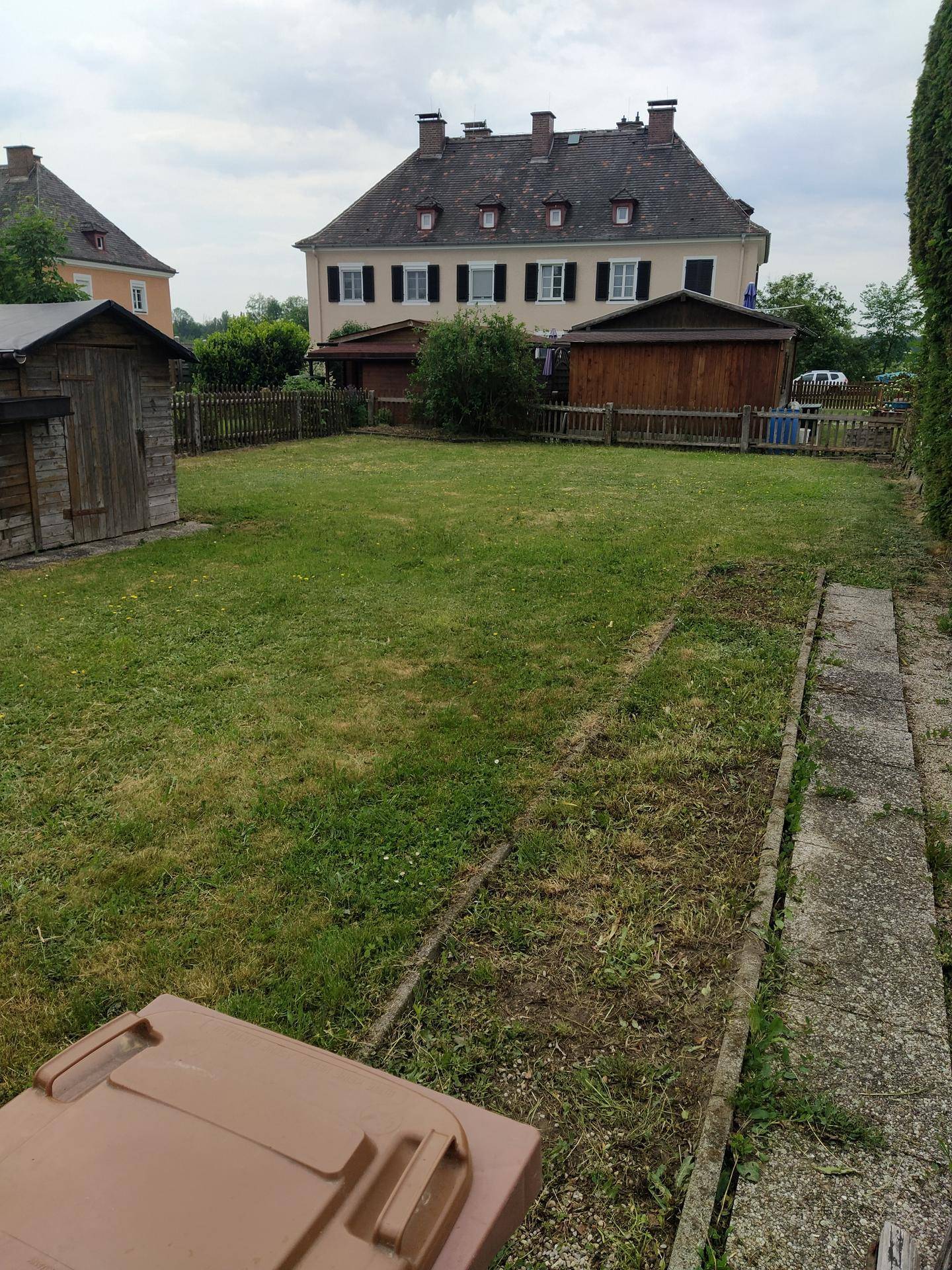 Großer Gartenbereich mit Rasenfläche, Gartenhäusern und Blick auf ein historisches Gebäude im Hintergrund.